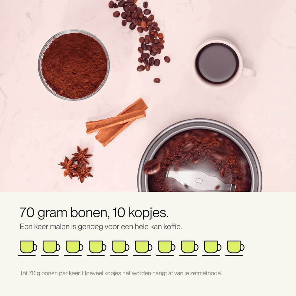 Coffee grinder, beans, grounds, a cup, cinnamon, and star anise on a light background.