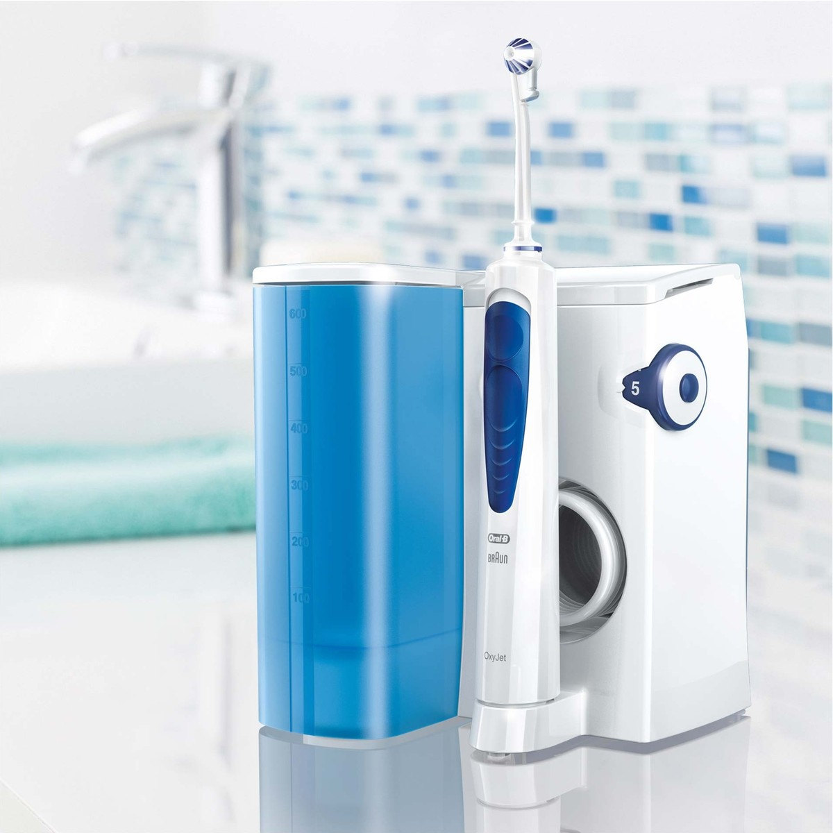 Mavi beyaz fayonlar önünde beyaz banyo tezgahında duran beyaz ve mavi Oral-B OxyJet ağız duşu.