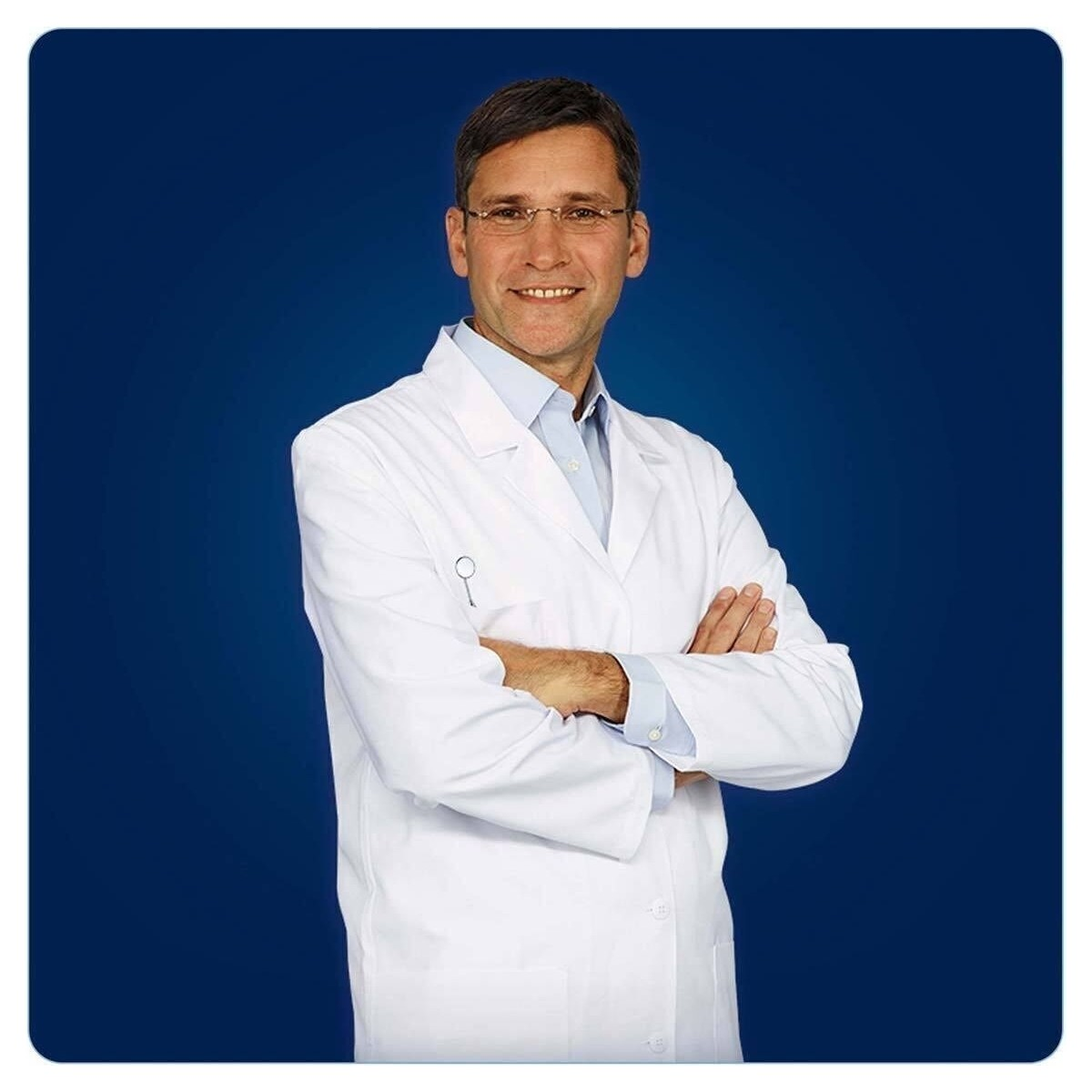 Beyaz önlüklü ve gözlüklü erkek doktor, mavi arka plan önünde kollarını kavuşturarak gülümsüyor.