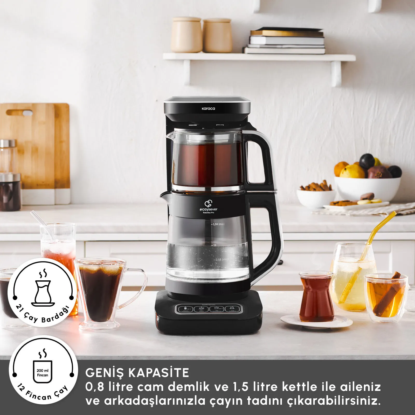 Mutfak tezgahında siyah bir çay makinesi, etrafında içecek bardakları ve arka planda yiyecekler duruyor.