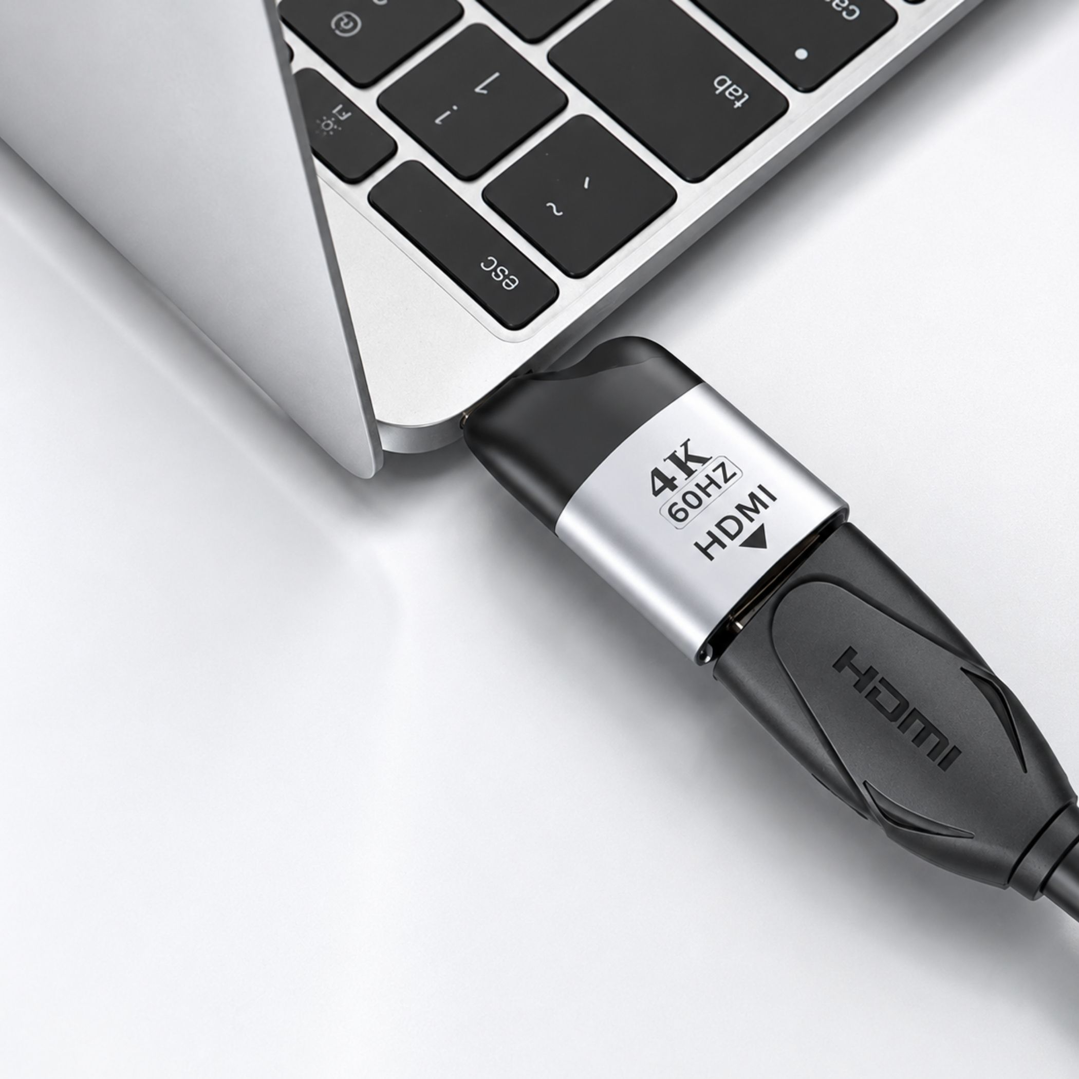 Ein schwarz-silberner 4K 60Hz HDMI-Adapter ist an der Seite eines silbernen Laptops angeschlossen.