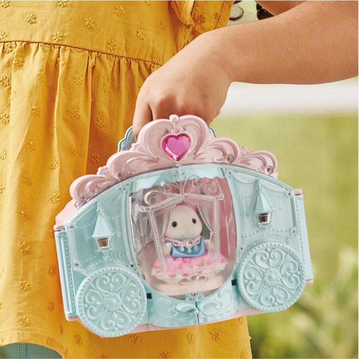 Ein Kind hält eine detailreiche, blau-rosa Spielzeugkutsche mit einer weißen Tierfigur im Inneren.