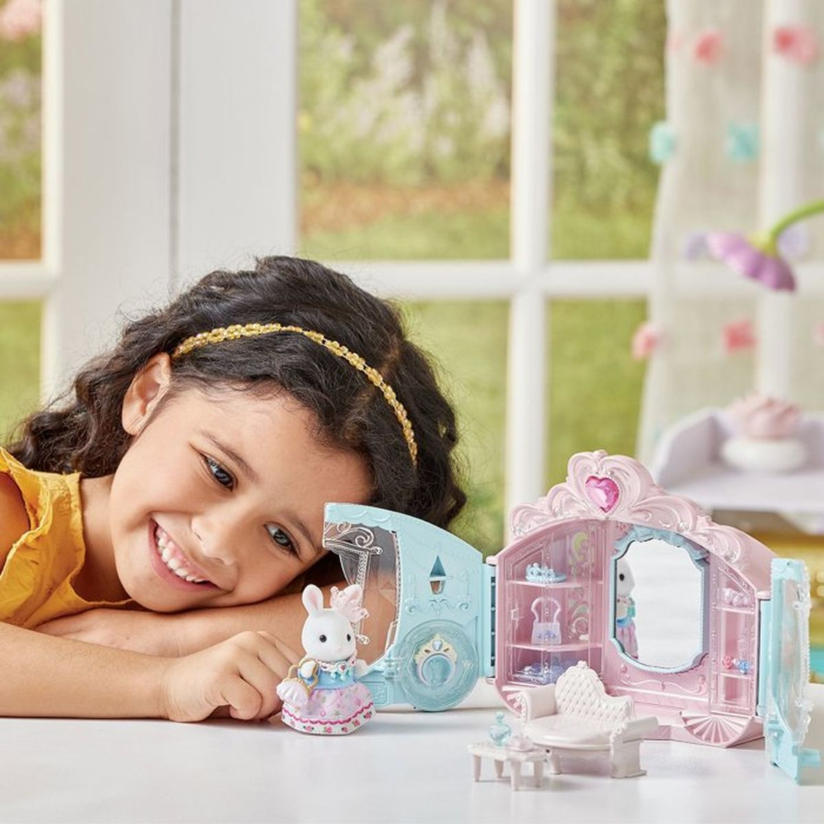 Ein junges Mädchen lächelt beim Spielen mit einer Hasenfigur und einem Kutschenspielset.