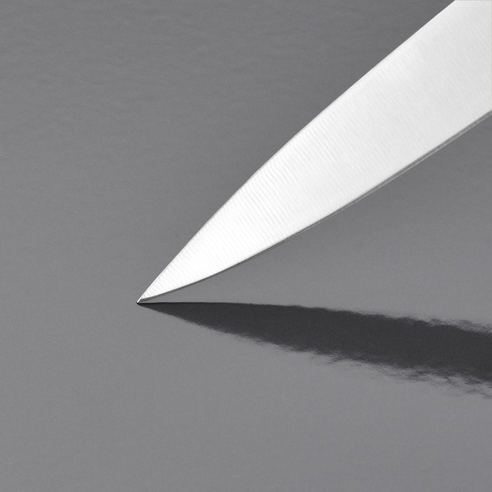 Die scharfe Klinge eines silbernen Messers ruht auf einer glatten, dunklen Oberfläche und wirft einen deutlichen Schatten.