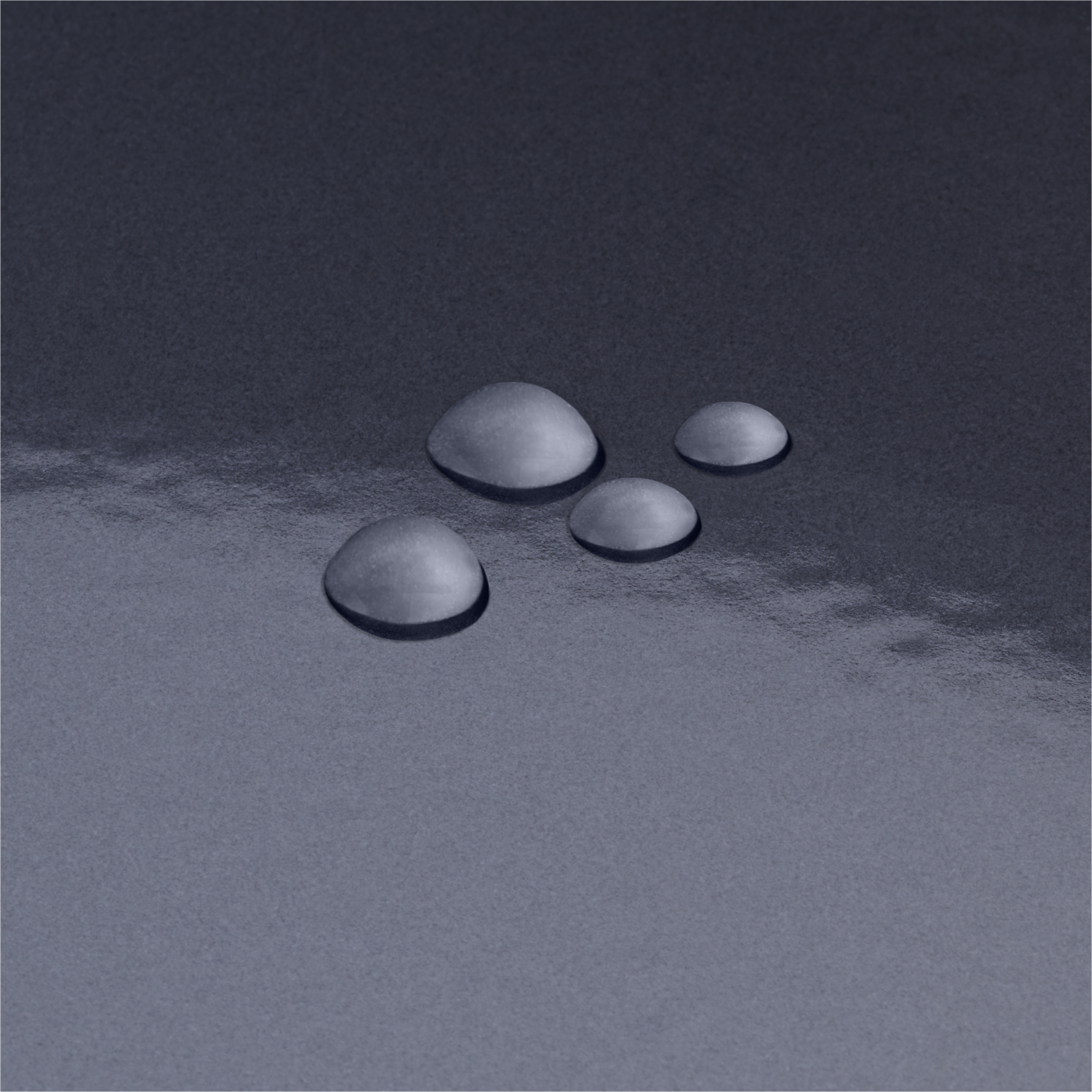 Vier glänzende Wassertropfen liegen auf einer glatten, dunkelgrauen Oberfläche mit subtilen Reflexionen.