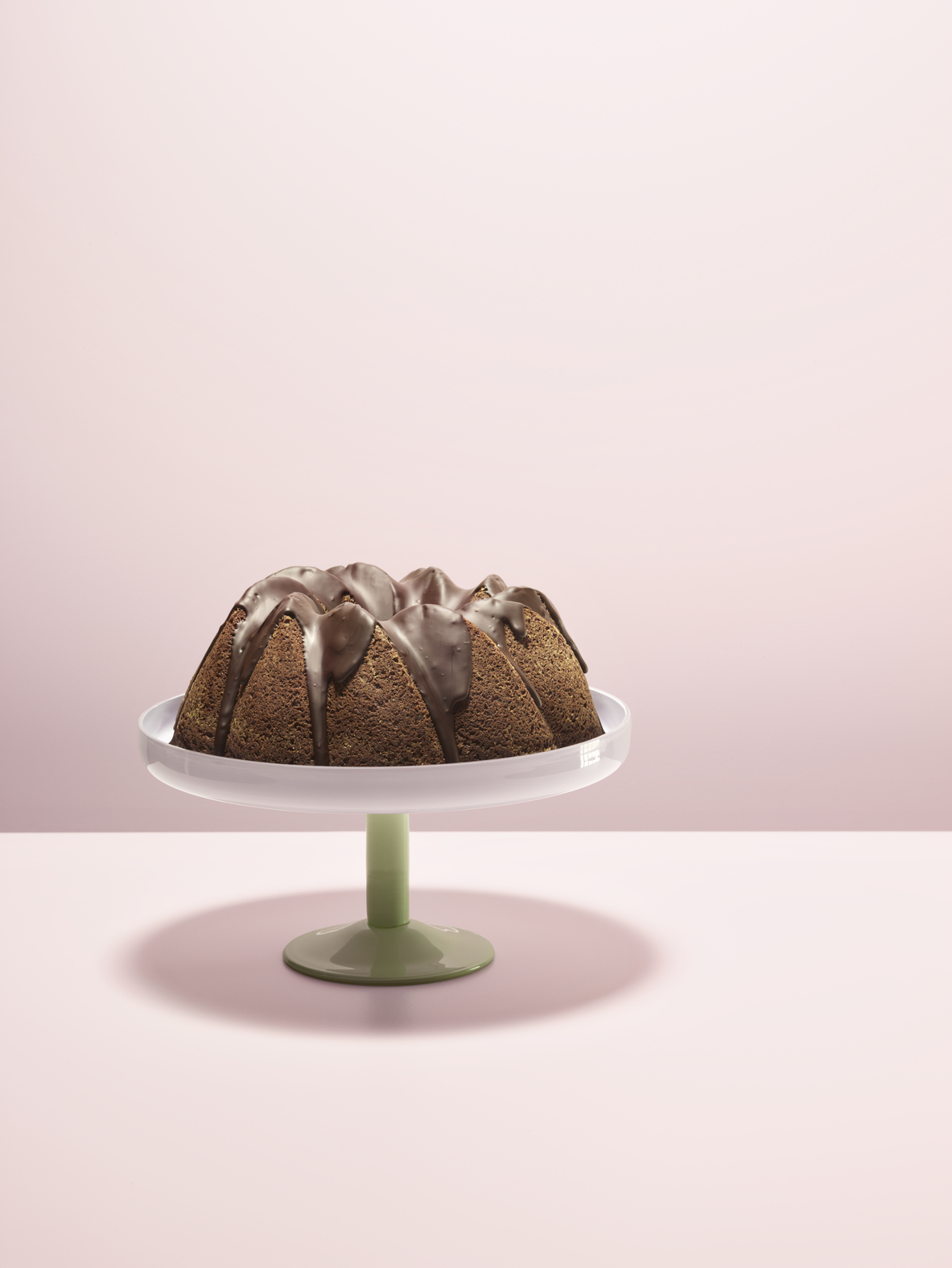 Babka z polewą czekoladową na zielonym stojaku na różowym tle.