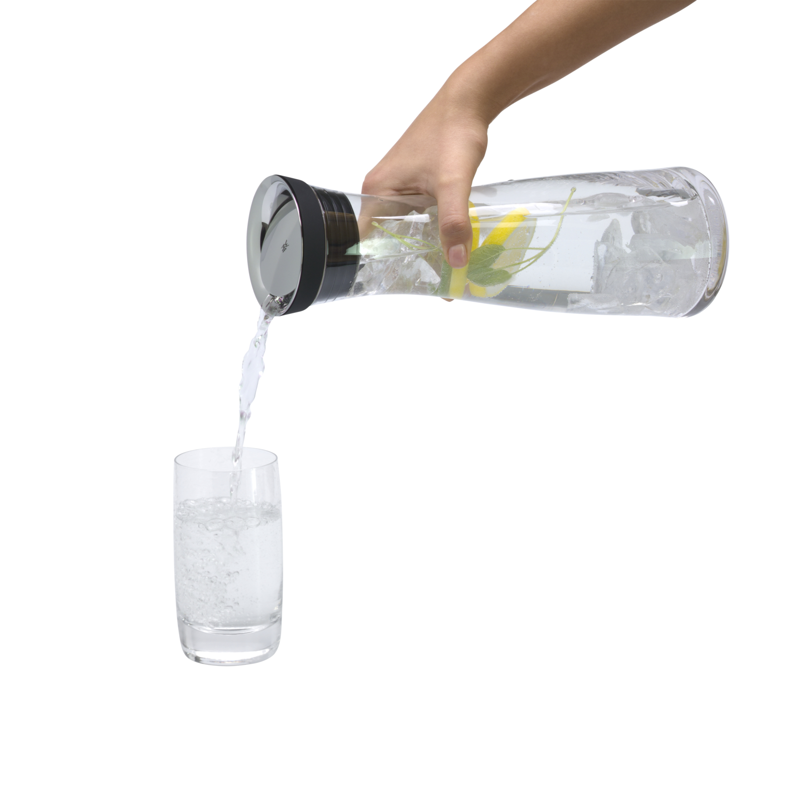 Eine Hand gießt Wasser mit Zitrone und Eis aus einer Glaskaraffe in ein Glas vor weißem Hintergrund.