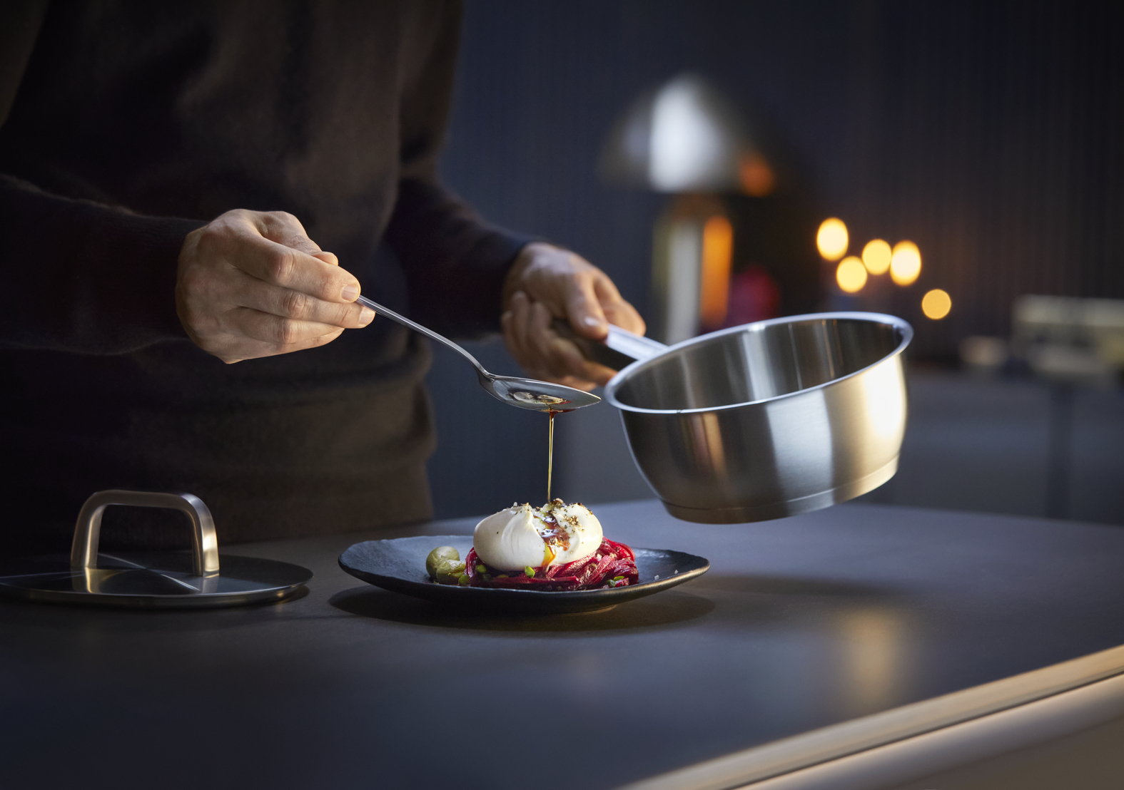 Ein Koch gießt Öl aus einem Löffel auf ein Gericht mit Burrata und Rote Bete.