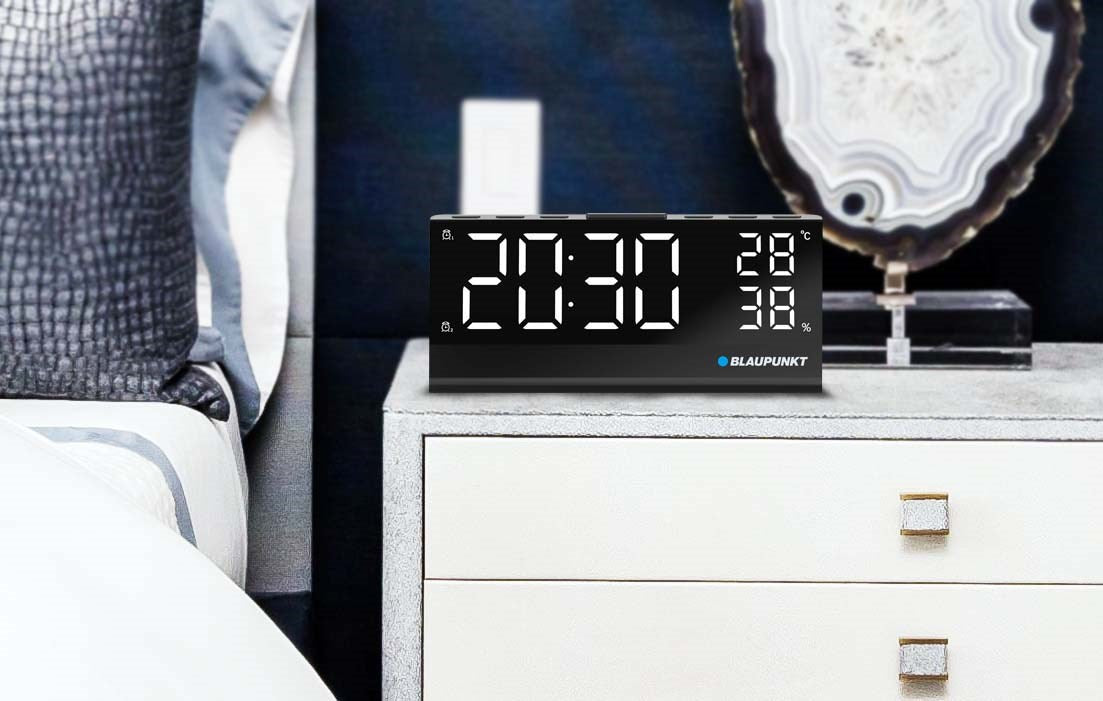 Una sveglia digitale Blaupunkt su un comodino bianco in una camera da letto moderna.