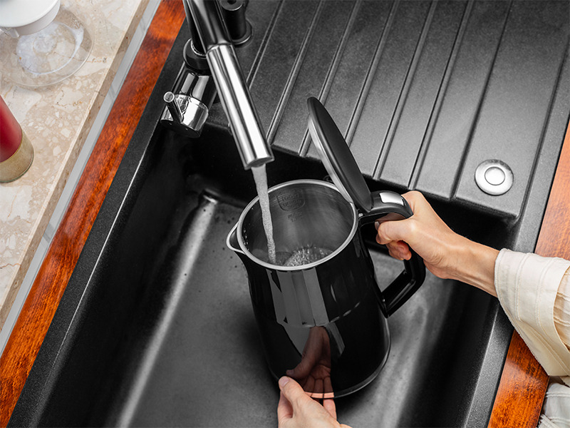 Una persona riempie un bollitore elettrico nero con acqua in un moderno lavello da cucina nero.