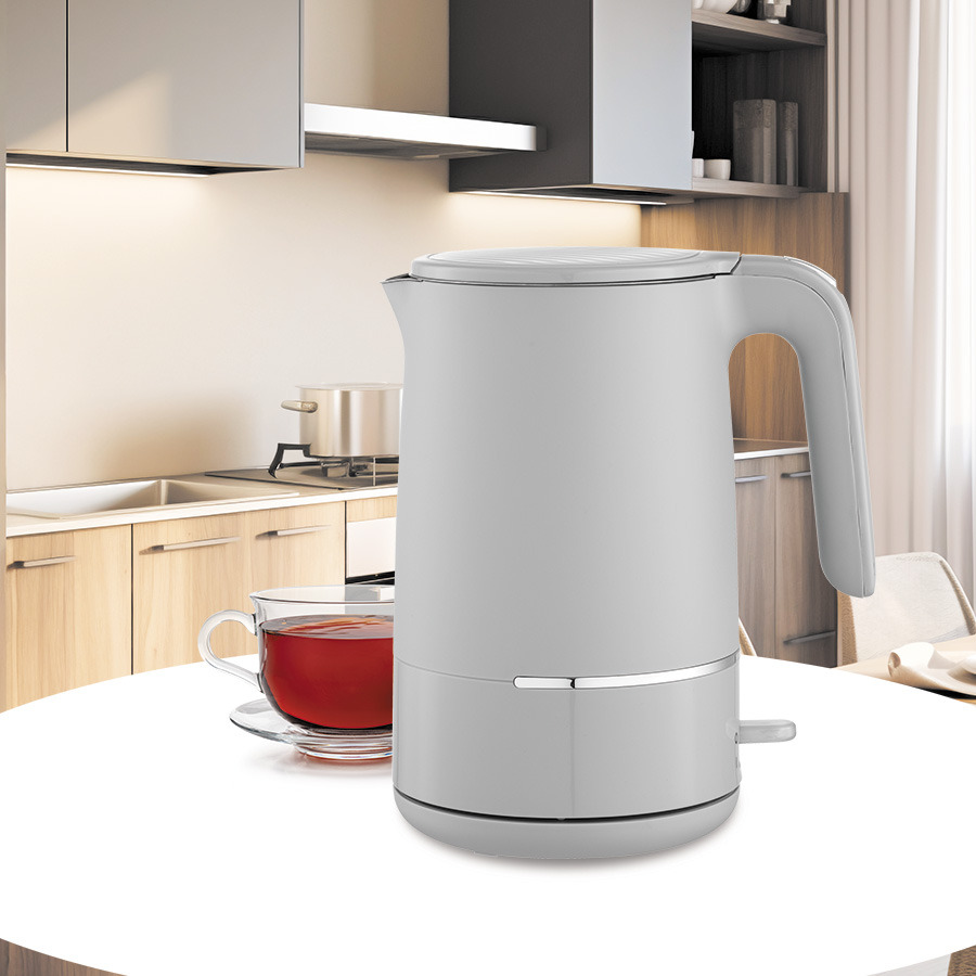 Un bollitore elettrico grigio e una tazza di tè si trovano su un tavolo bianco in una cucina moderna.