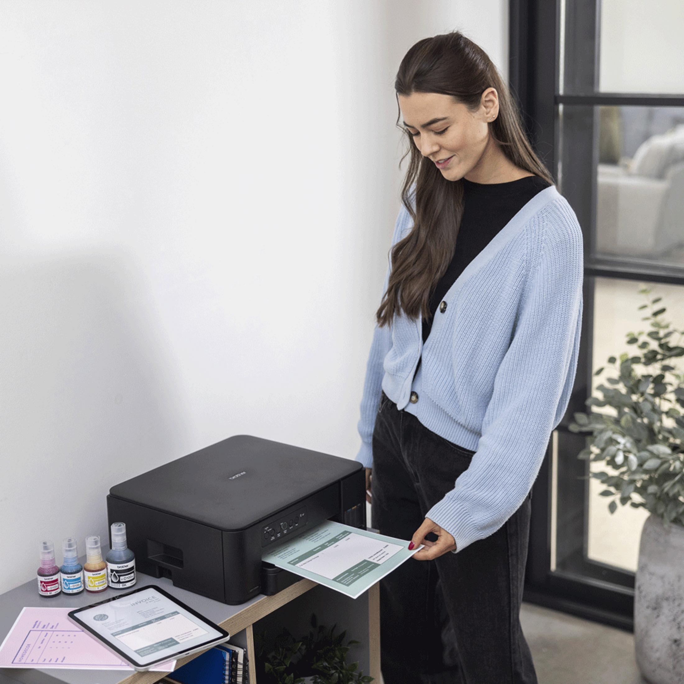 Eine Frau in blauer Strickjacke nimmt ein gedrucktes Dokument aus einem schwarzen Drucker.