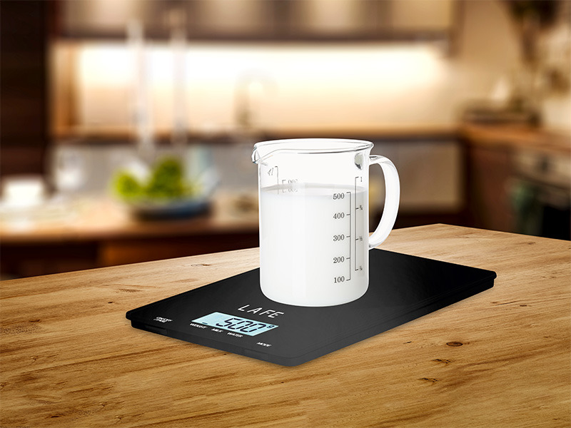 Ein Glas mit Milch steht auf einer schwarzen Küchenwaage auf einem Holztisch.