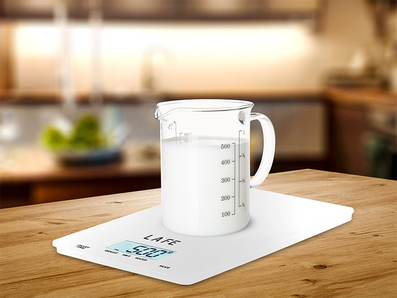 Ein Glasmessbecher mit Milch steht auf einer weißen digitalen Küchenwaage auf einem Holztisch.