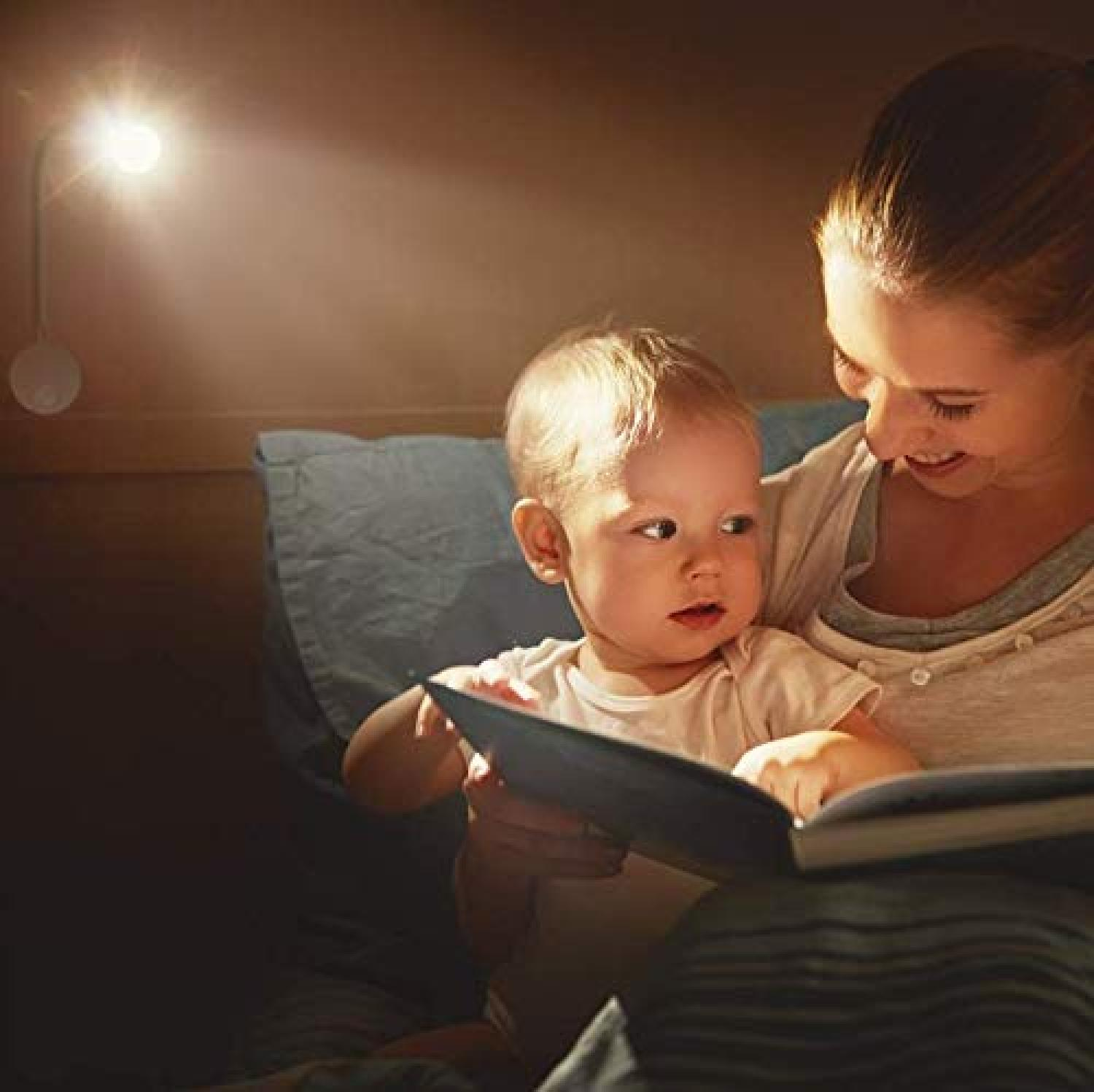 Eine Mutter liest ihrem kleinen Kind im Bett bei gedimmtem Wandlampenlicht ein Buch vor.
