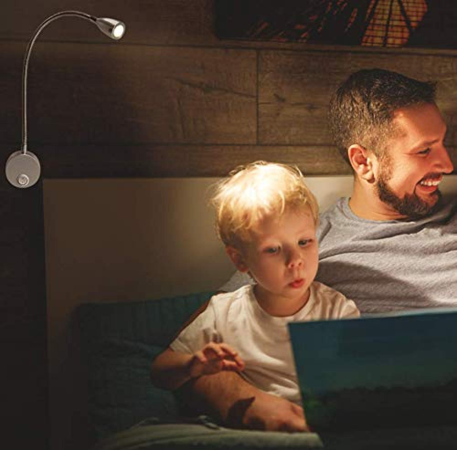 Ein Vater und sein Sohn lesen ein Buch im Bett, beleuchtet von einer Wandlampe.