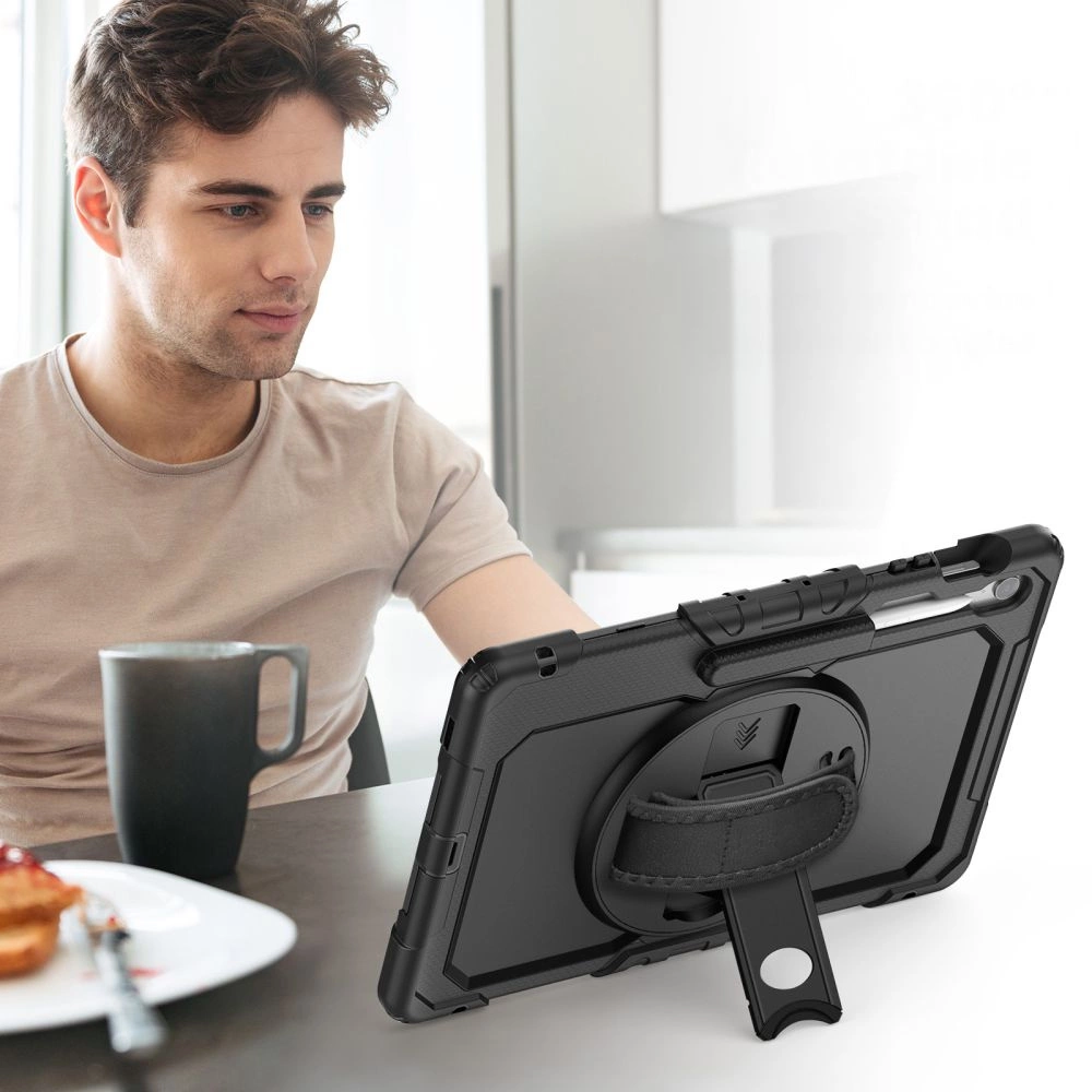 Ein Mann sitzt an einem Tisch mit Tasse und Kuchen, während vor ihm ein Tablet in schwarzer Schutzhülle steht.