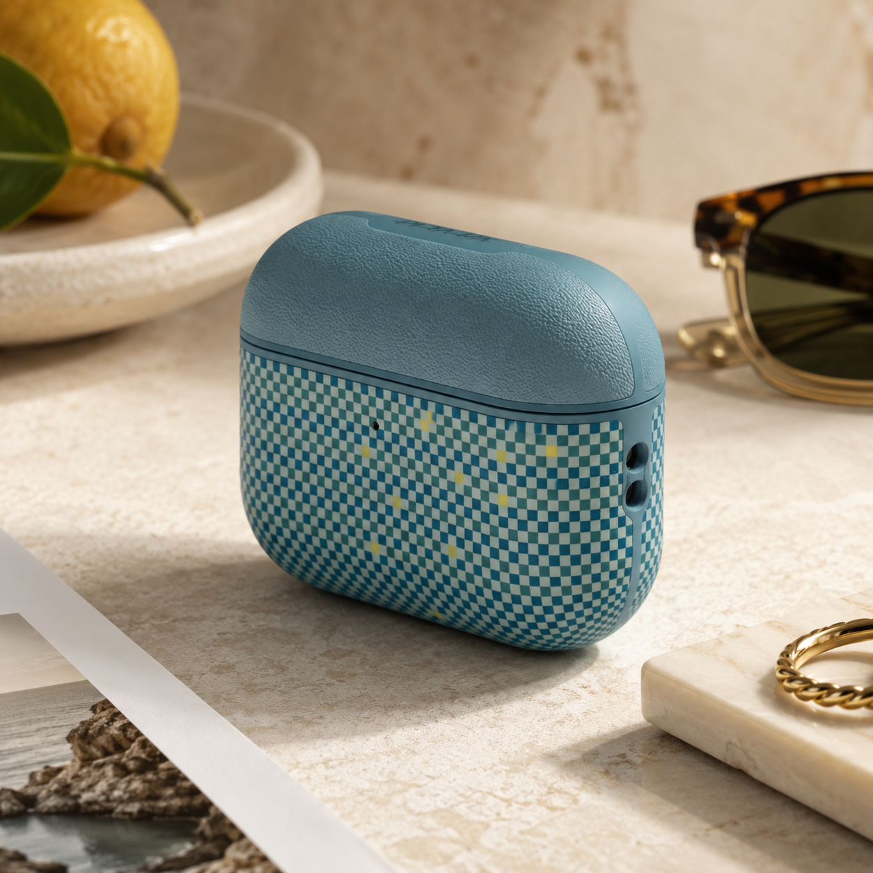 Estuche de auriculares azul a cuadros en una mesa con limón y gafas de sol.