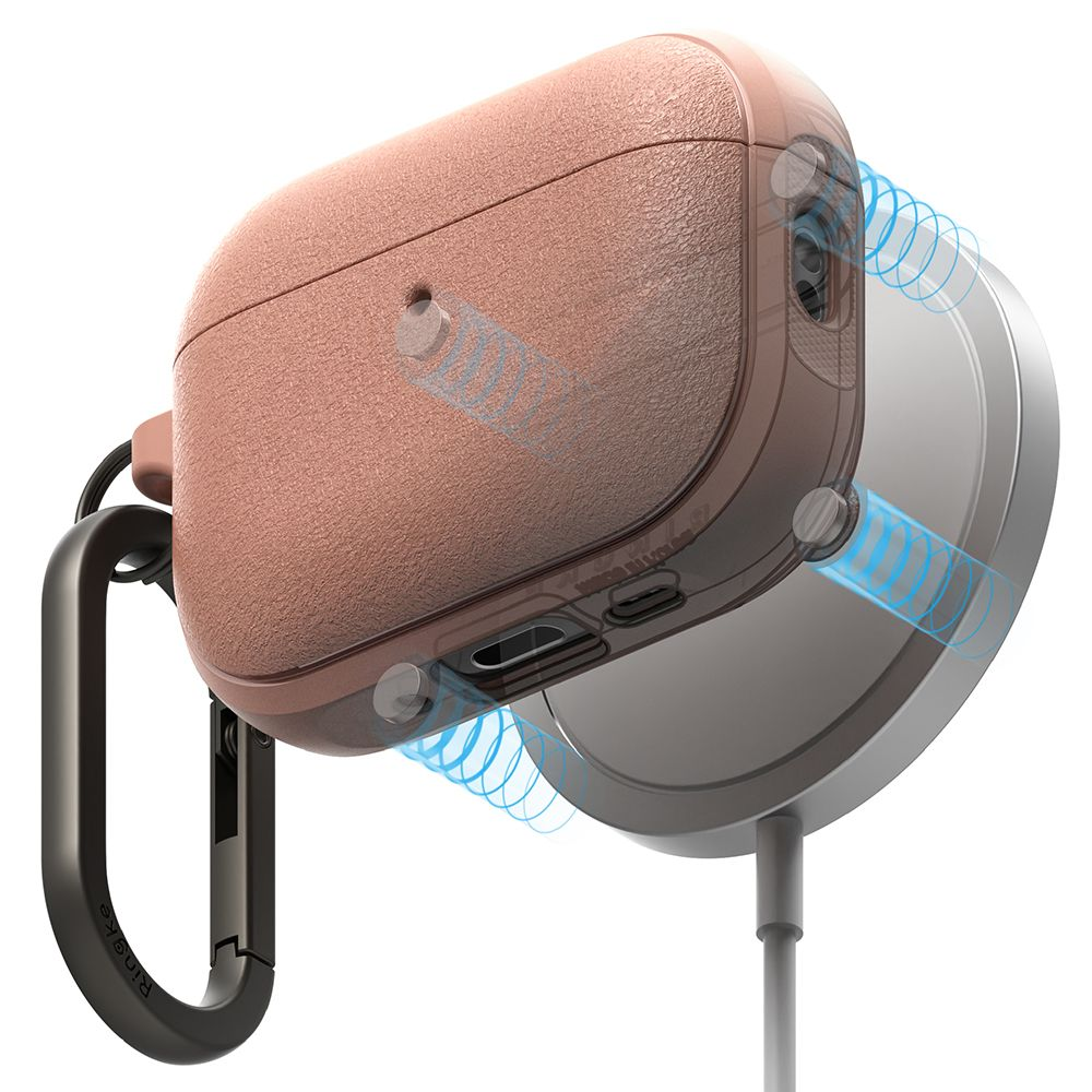 Una custodia rosa per AirPods Pro con moschettone è posizionata vicino a un caricabatterie MagSafe rotondo e argento.