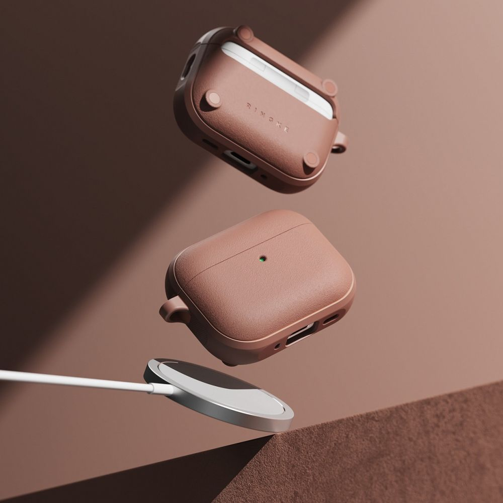 Due custodie per AirPods marroni e un caricatore bianco fluttuano su sfondo marrone.