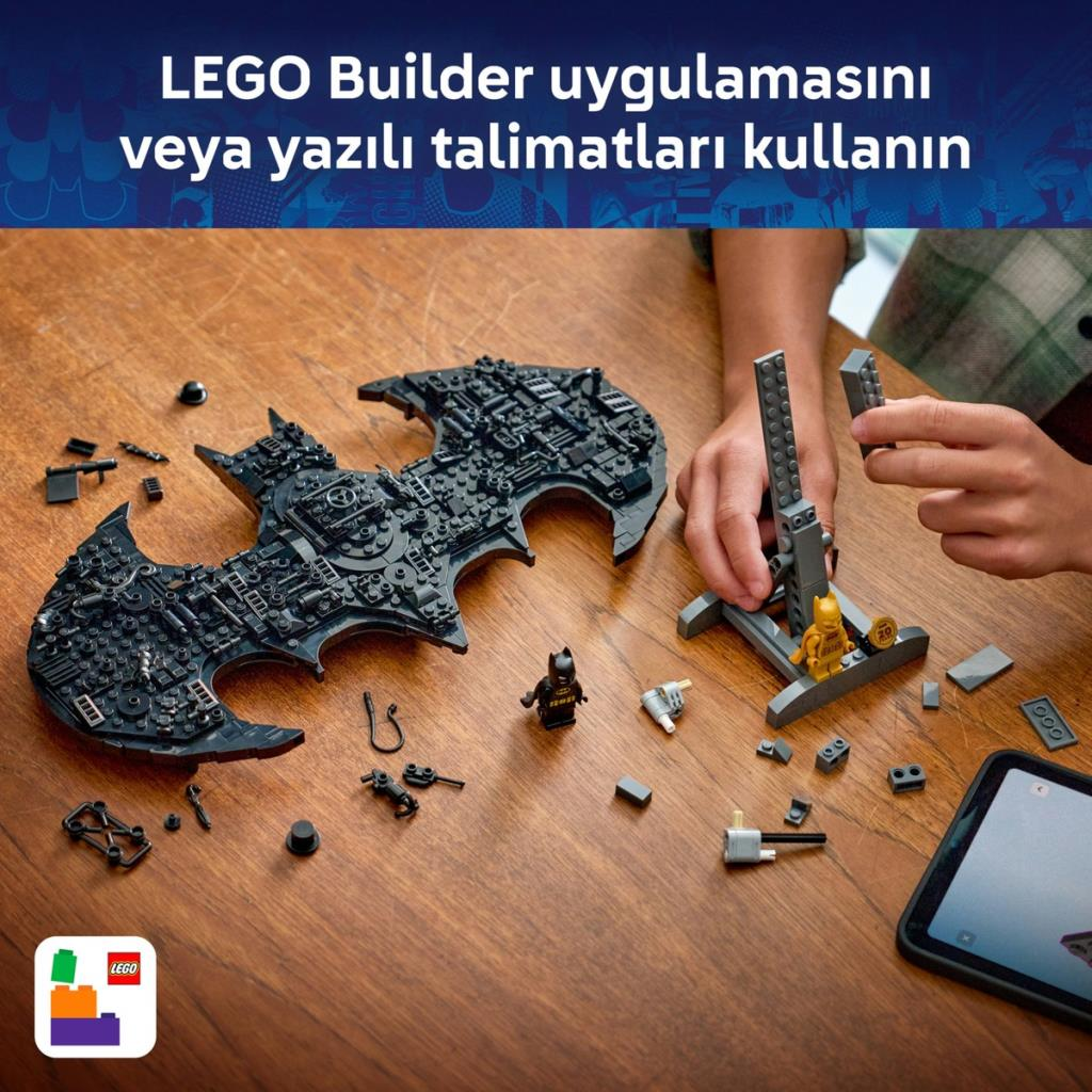 Bir kişi ahşap masa üzerinde talimatlarla Lego Batmobile birleştiriyor.