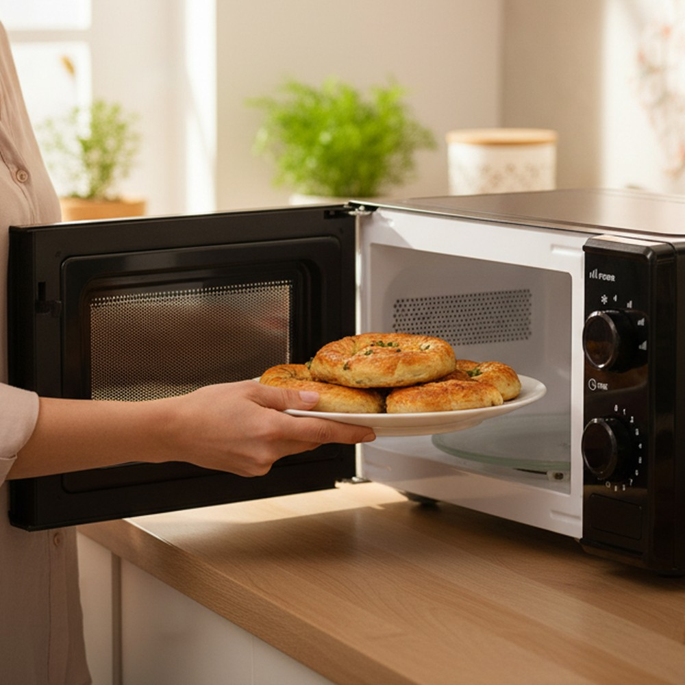 Bir kadın tezgahtaki açık mikrodalgaya bir tabak çörek yerleştiriyor.