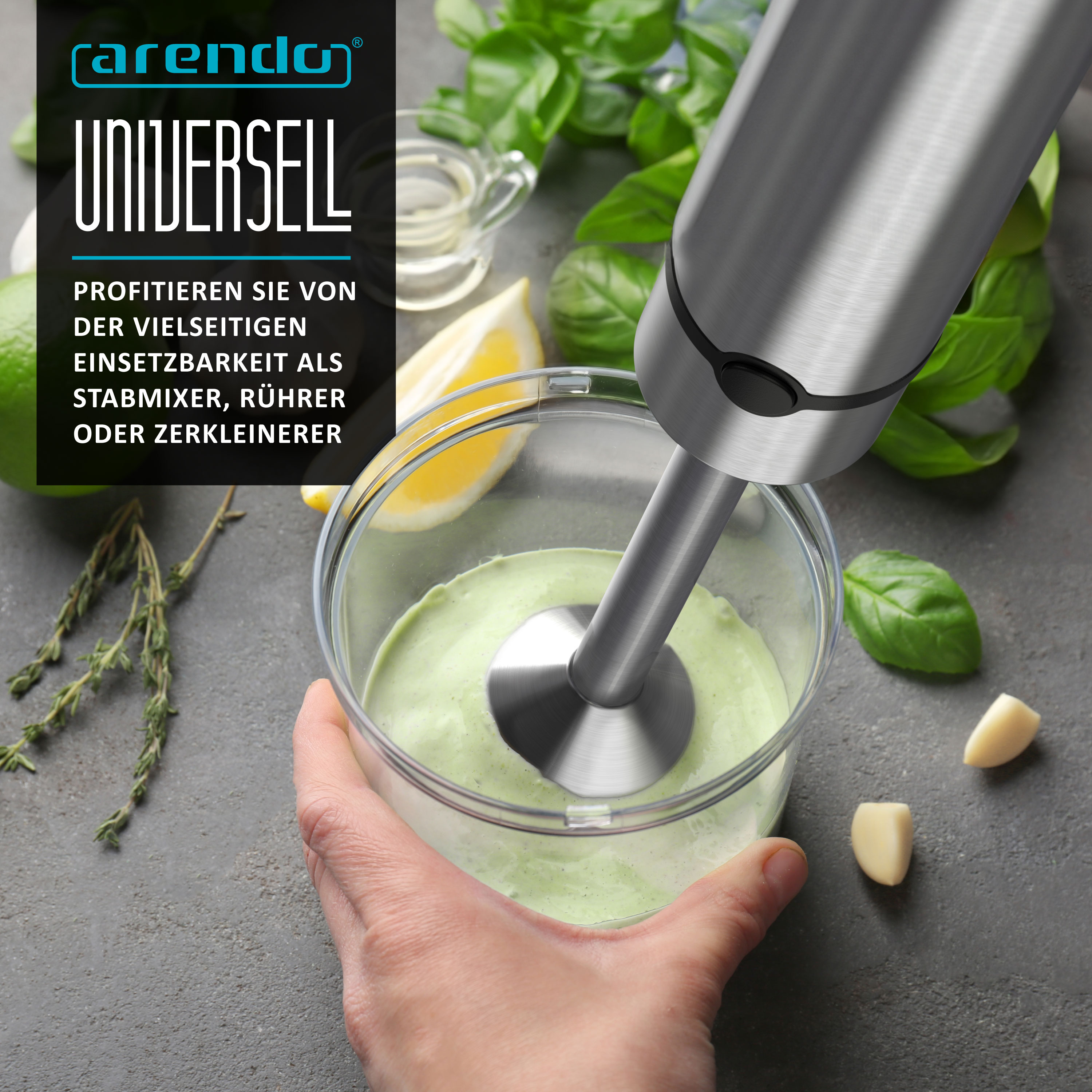 Stabmixer in Becher mit grüner Creme, umgeben von Kräutern, Zitrone und Knoblauch.