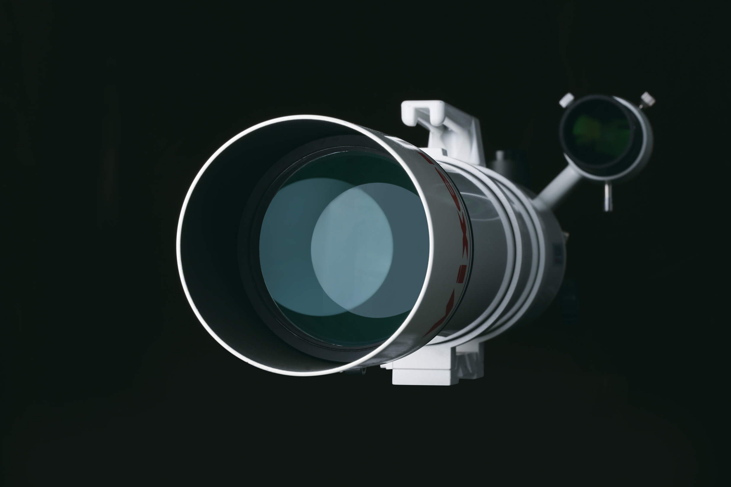 Un telescopio blanco con una gran lente frontal sobre fondo negro.