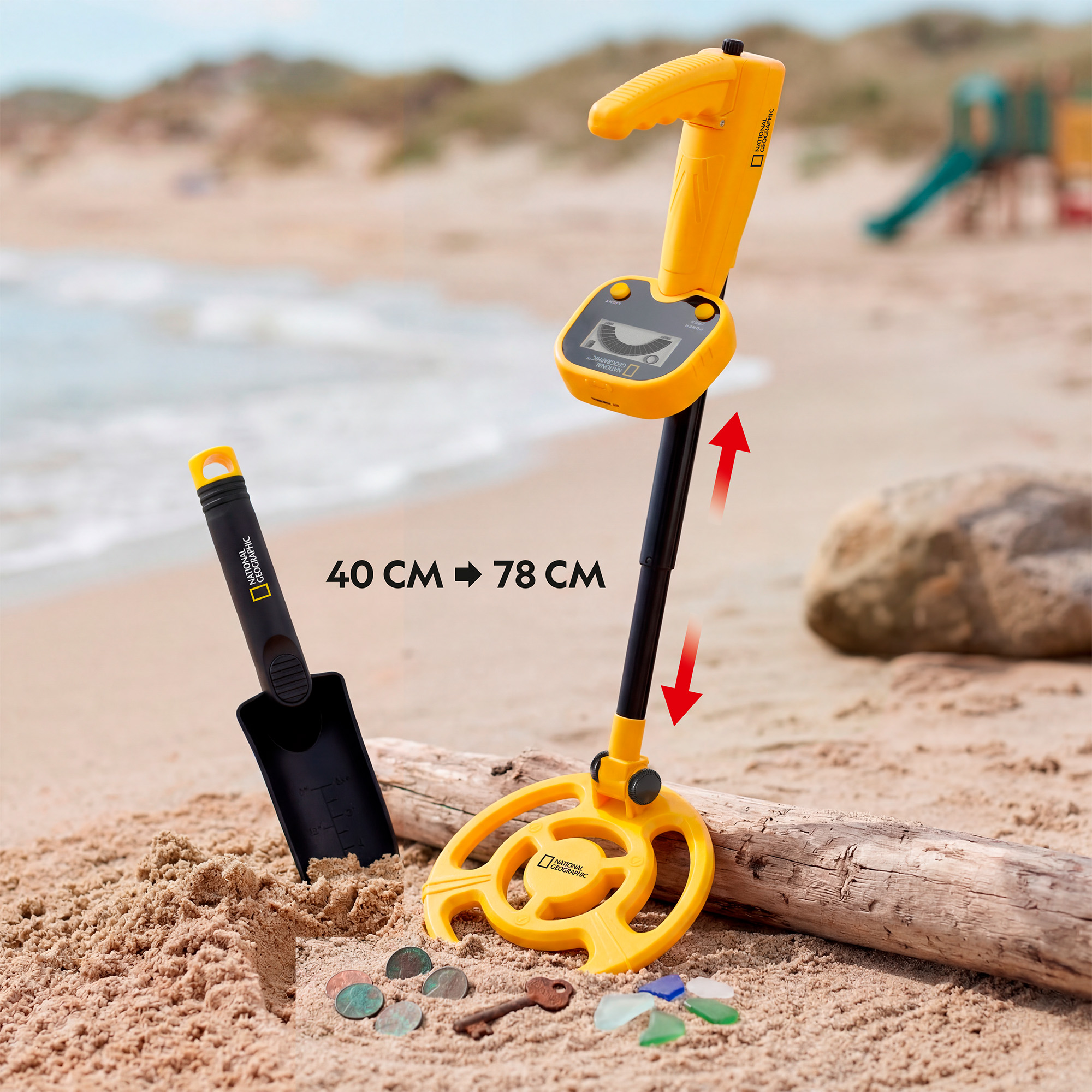 Un detector de metales amarillo y negro, una pala y monedas en la playa.