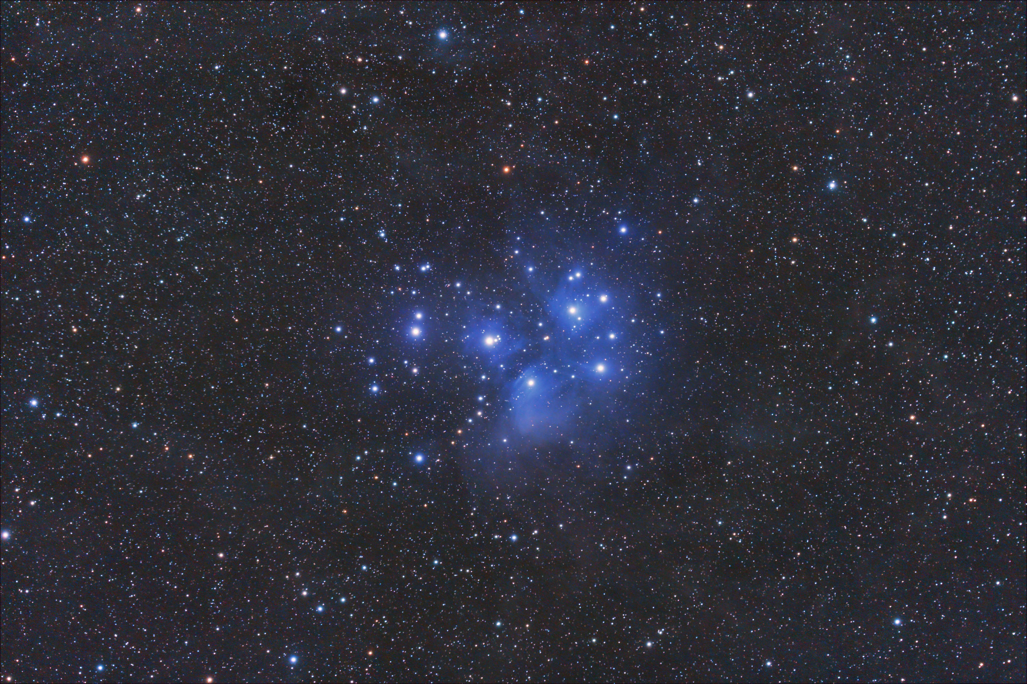 El cúmulo estelar de las Pléyades brilla en azul brillante en medio de un vasto campo de estrellas en el espacio oscuro.