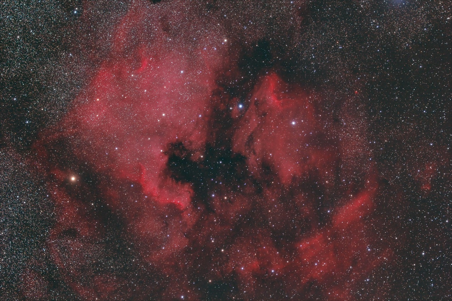 Nebulosa cósmica con regiones rojas de hidrógeno alfa, oscuras nubes de polvo y numerosas estrellas blancas.
