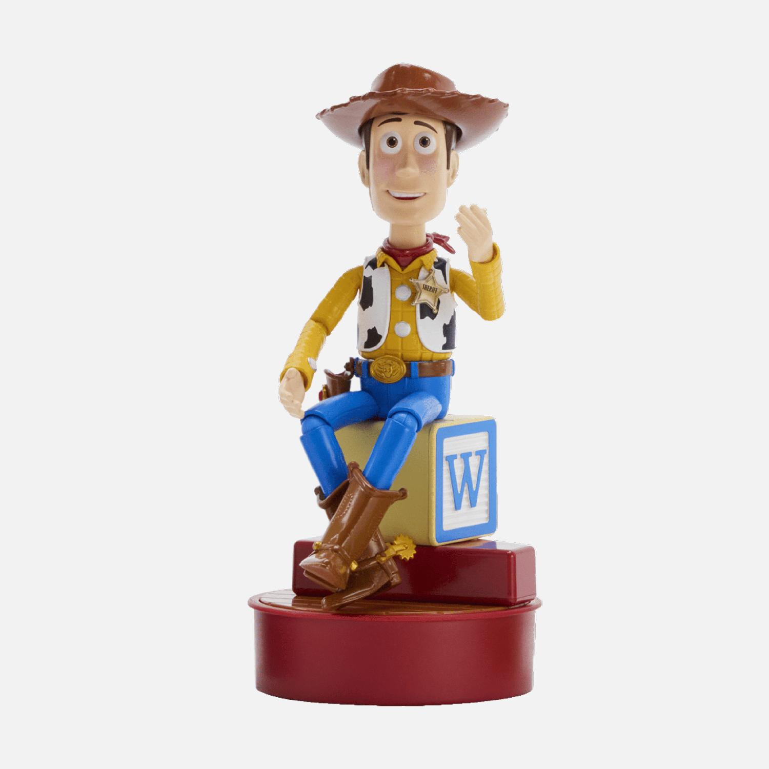 Figura de juguete Woody de Toy Story sentado en un bloque con una letra W, sobre una base roja.