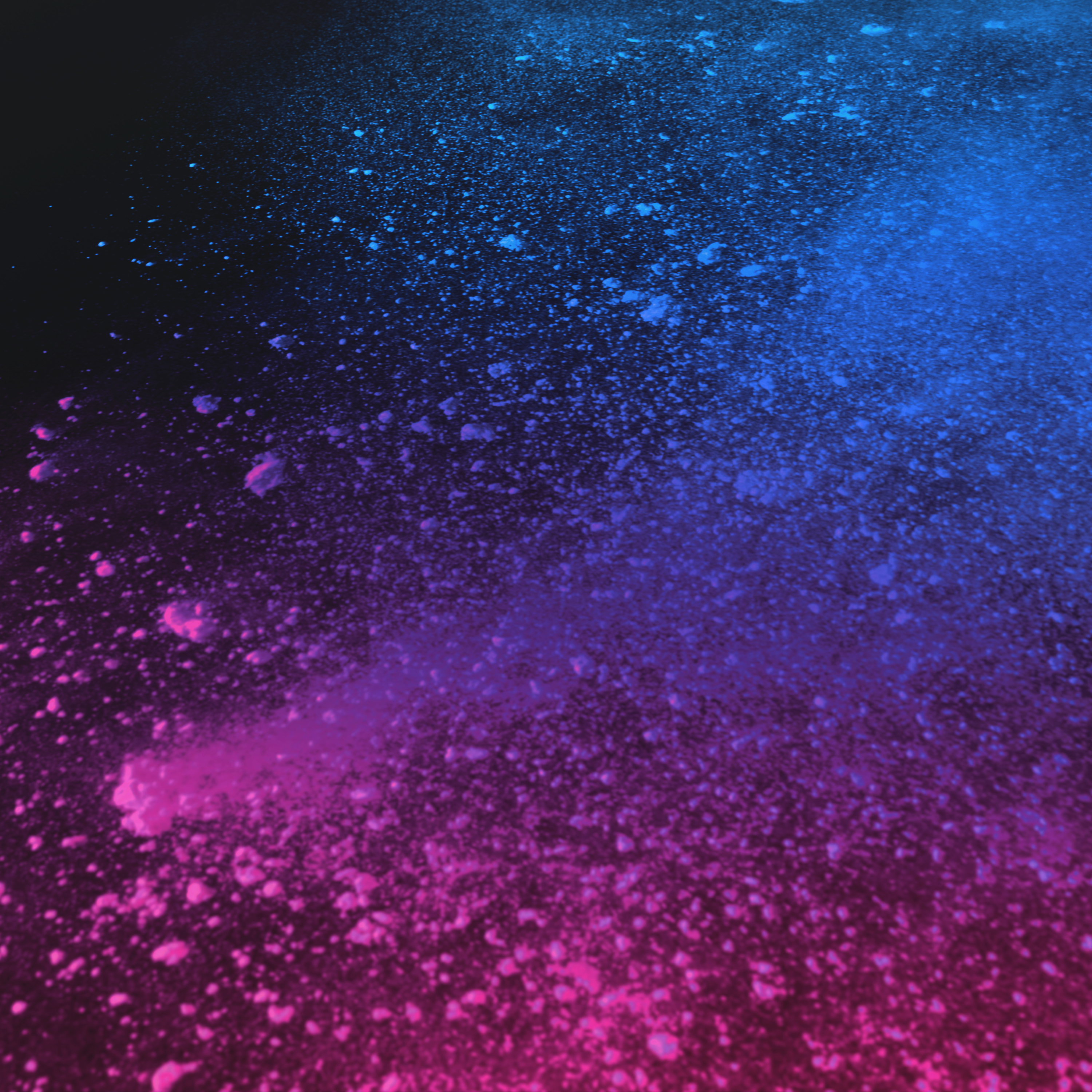 Blaue und pinke Pulverpartikel schweben auf dunklem Hintergrund.