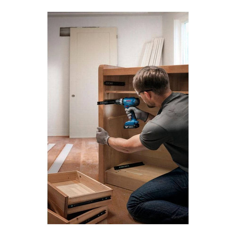 Un artigiano usa un trapano a batteria blu per installare guide in un mobile di legno.