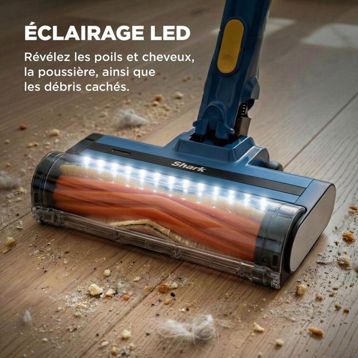 Testina aspirapolvere Shark con luci LED luminose su pavimento in legno con detriti.