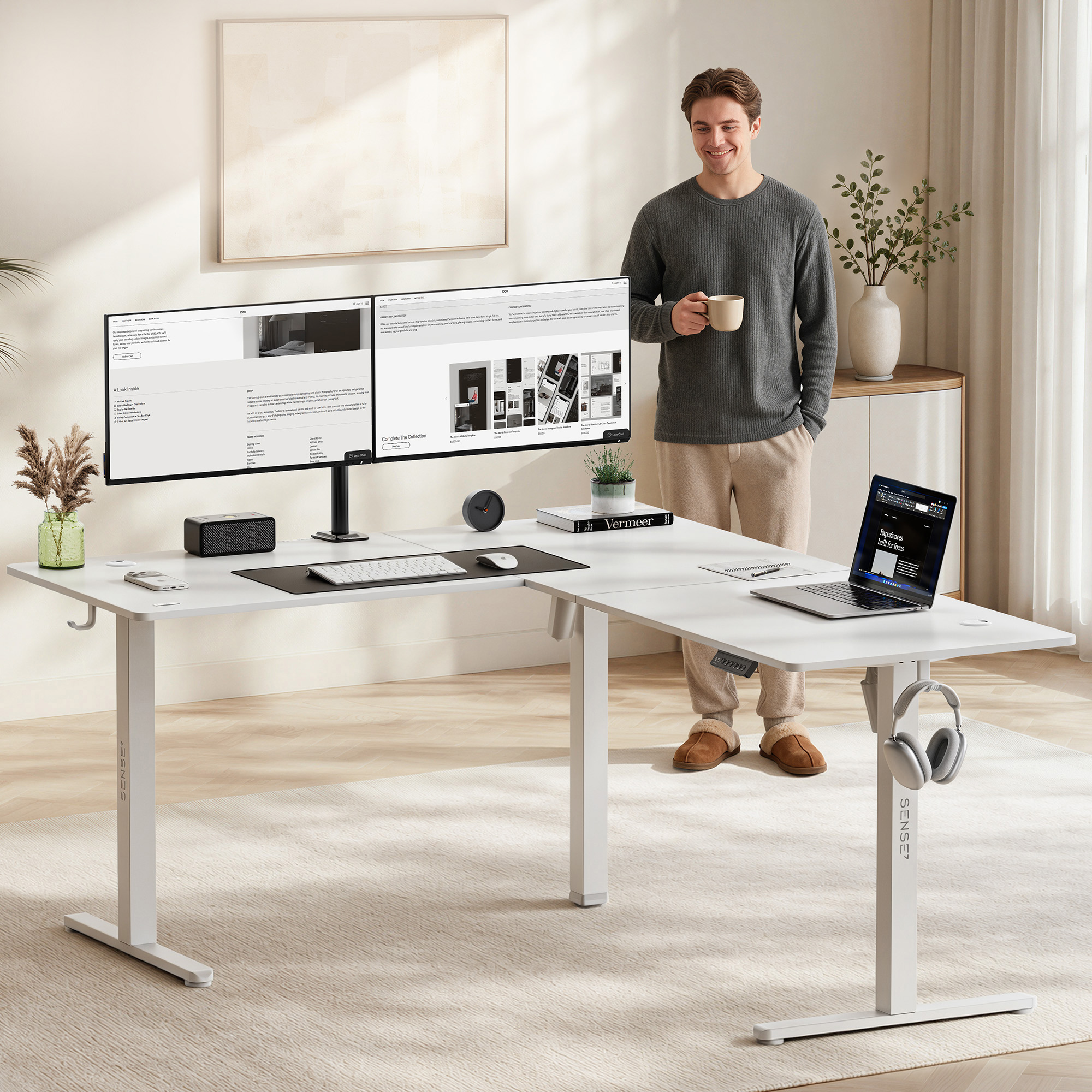Un uomo sorridente con caffè si trova in ufficio vicino a una grande scrivania angolare bianca con due monitor.