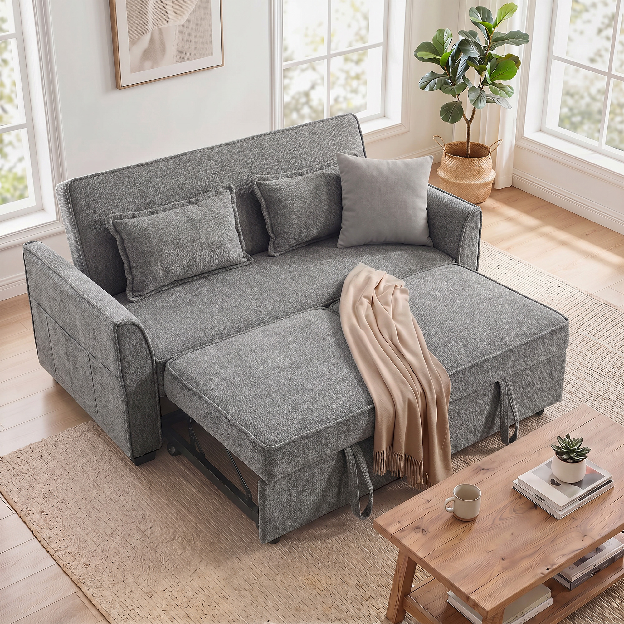 Un sofá cama gris con tres cojines y una manta beige sobre una alfombra en una sala de estar luminosa.