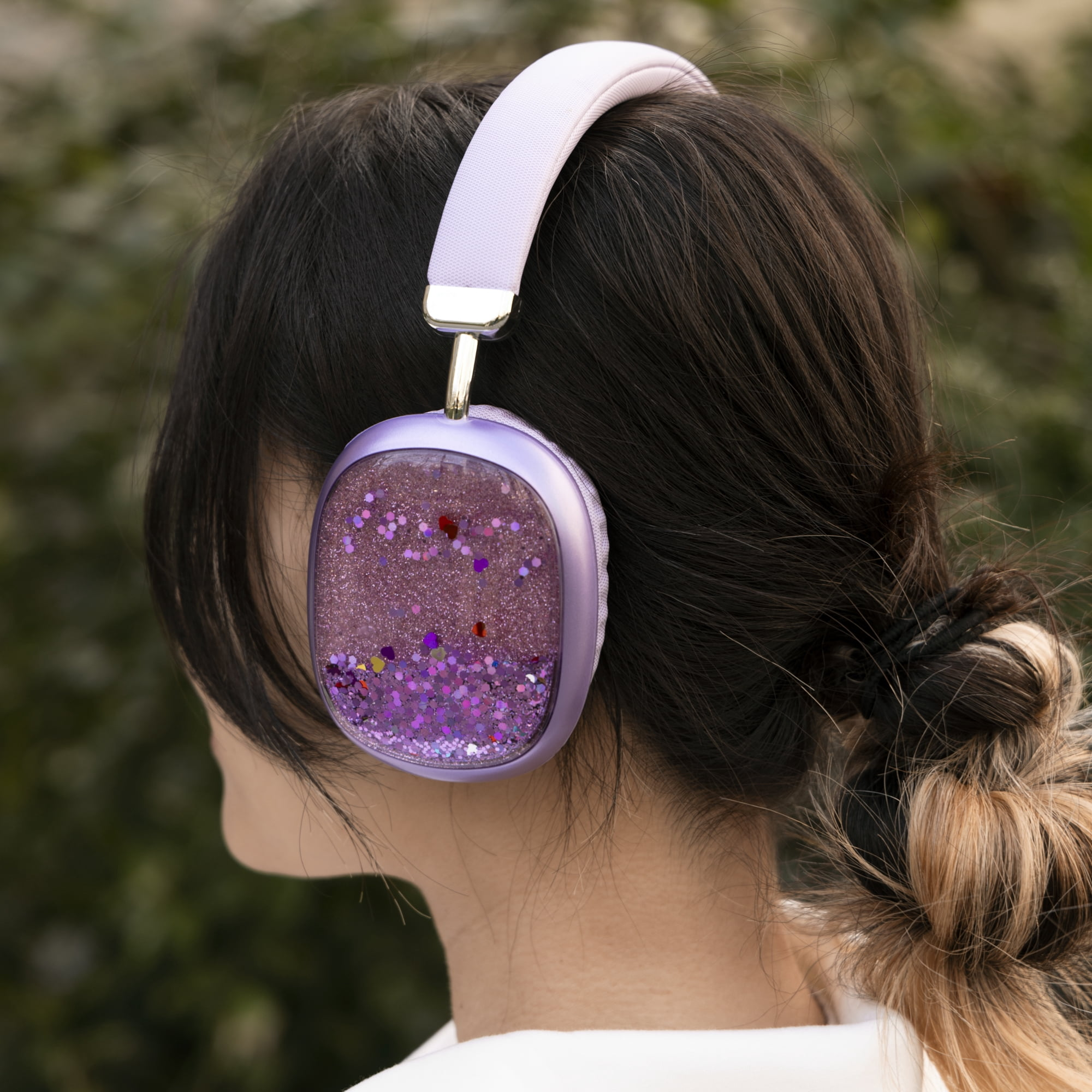 Eine Frau mit dunklem Haar trägt violette Glitzer-Kopfhörer vor grünem Hintergrund.