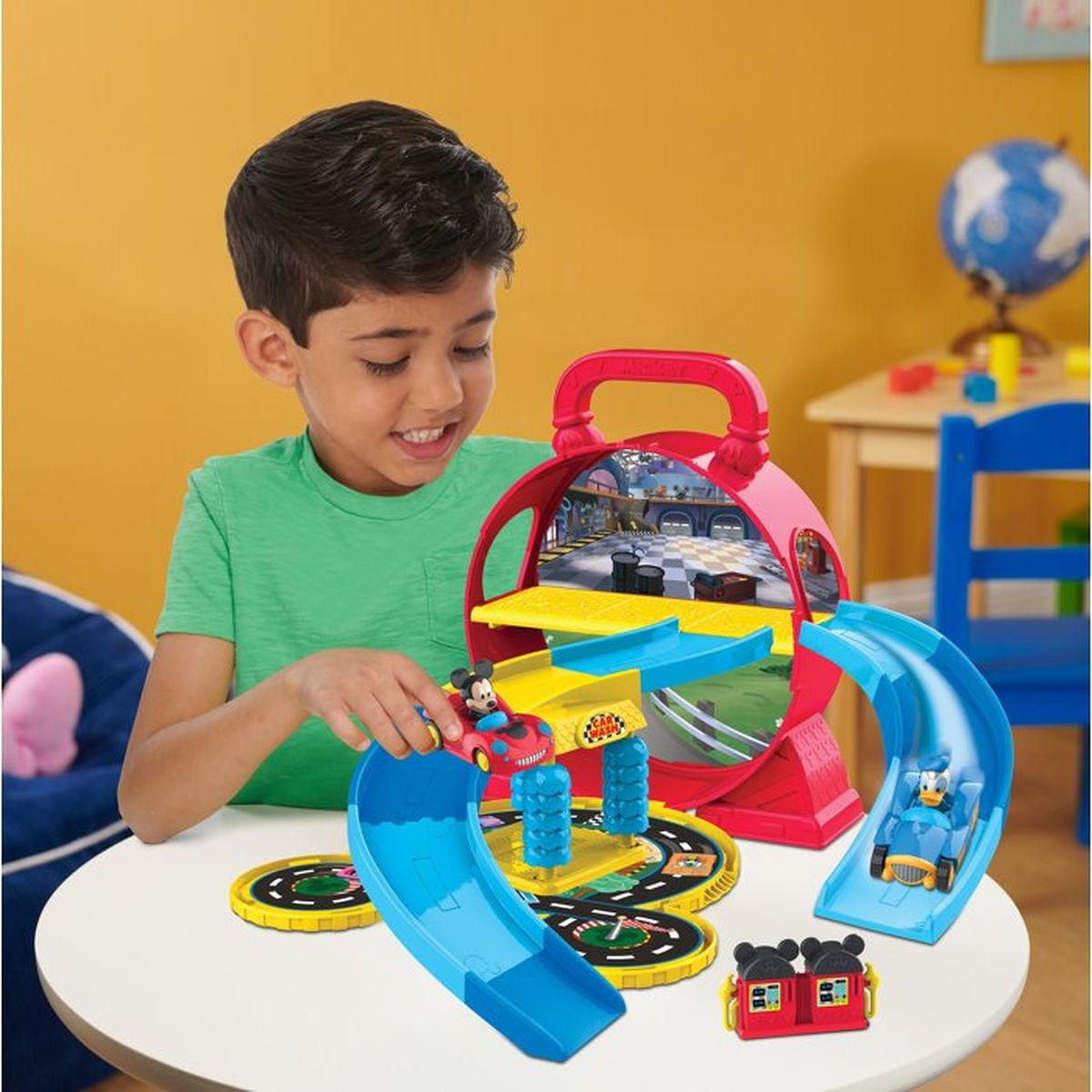 Ein Junge in einem grünen Shirt spielt am Tisch mit einem bunten Mickey-Maus-Spielset mit Autos und Rutschen.