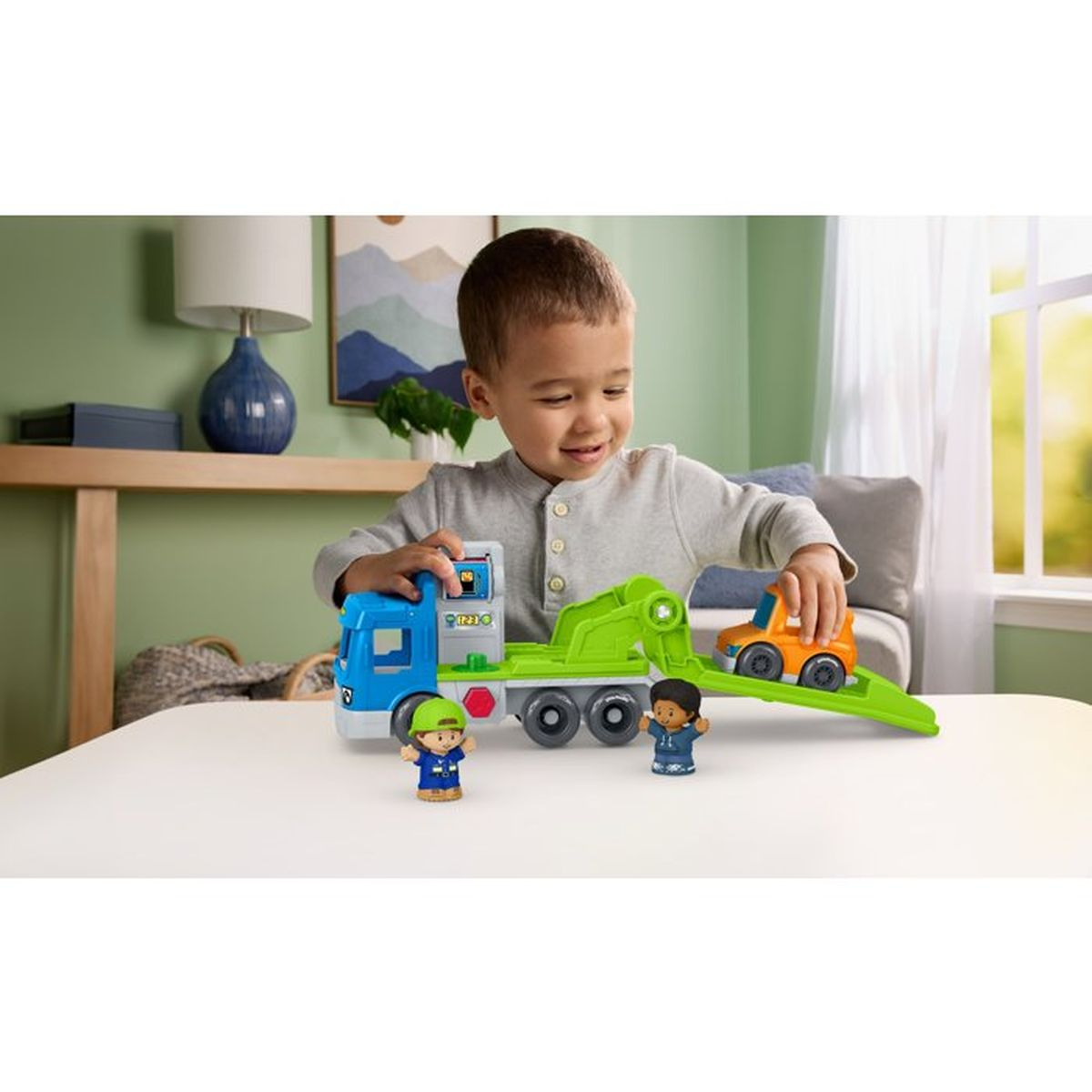 Ein kleiner Junge spielt mit einem blau-grünen Spielzeuglastwagen und rollt ein orangefarbenes Auto eine Rampe hinab.
