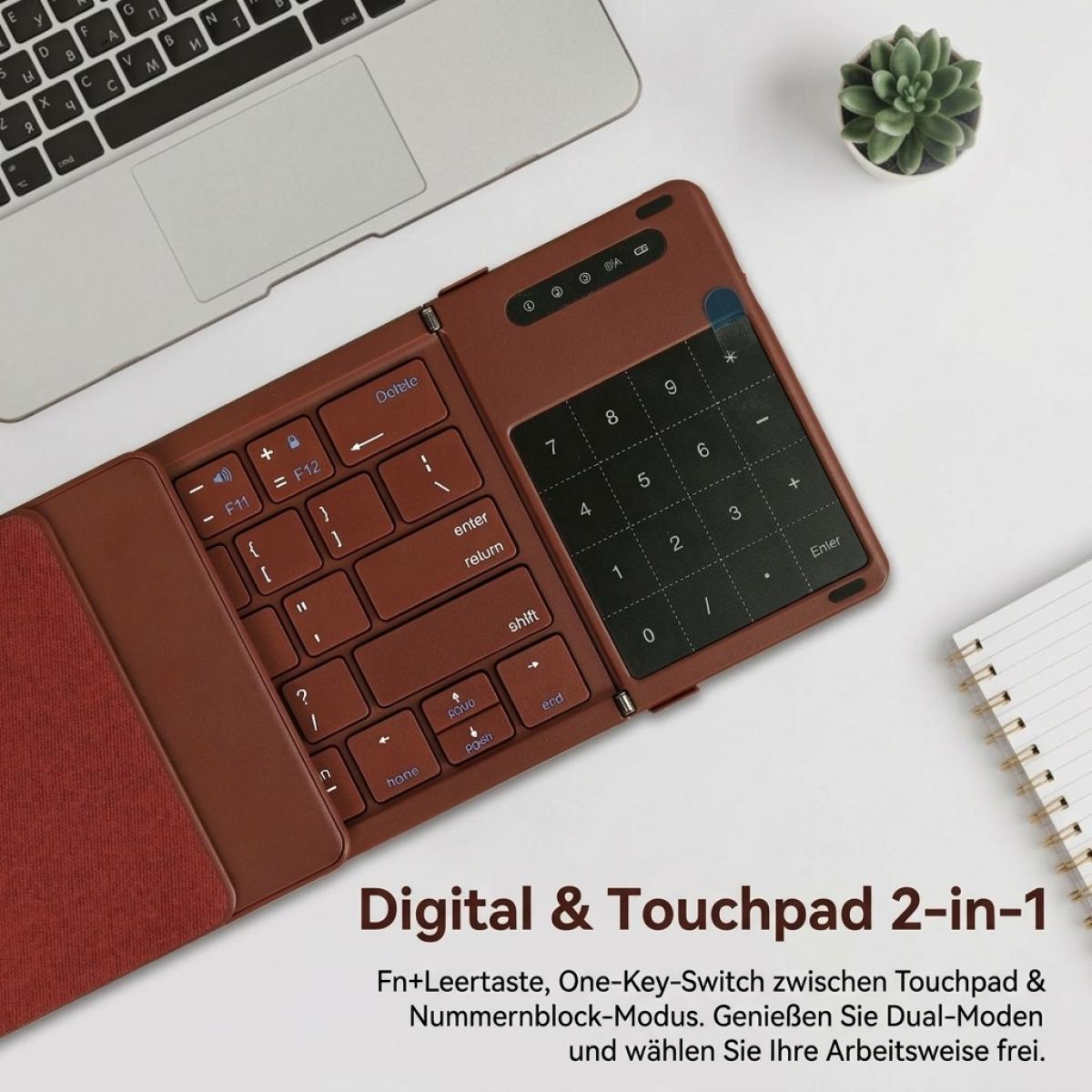 Eine braune Klapptastatur mit Touchpad und Ziffernblock neben Laptop, Notizbuch und Pflanze.