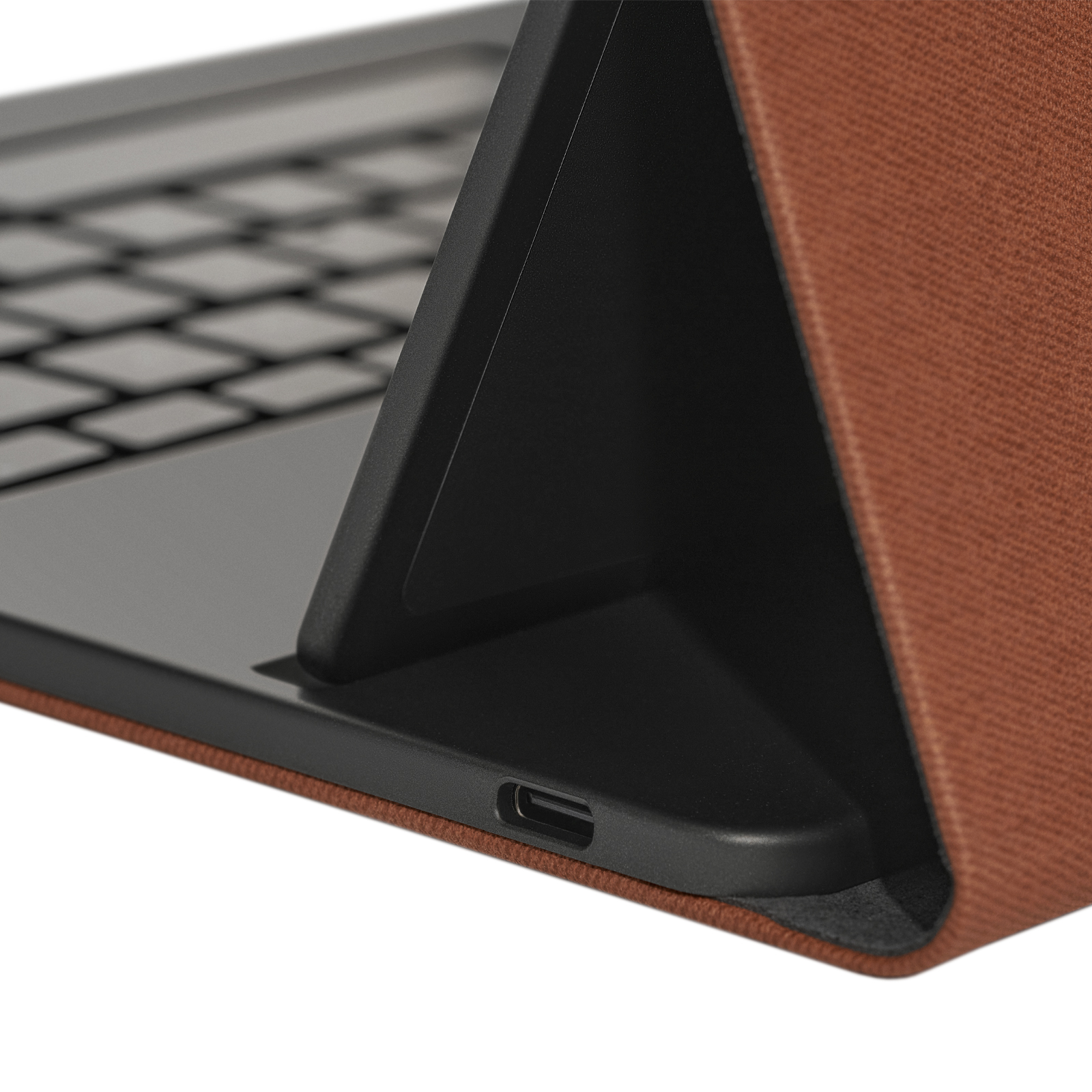 Primer plano de un teclado oscuro y un soporte de cuero marrón sobre fondo blanco con puerto USB-C.