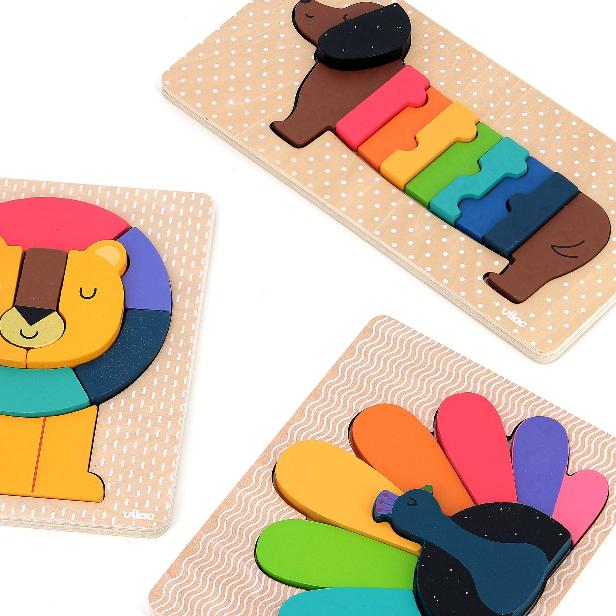 Drei bunte Holzpuzzle mit einem Hund, einem Löwen und einem Pfau auf weißem Grund.