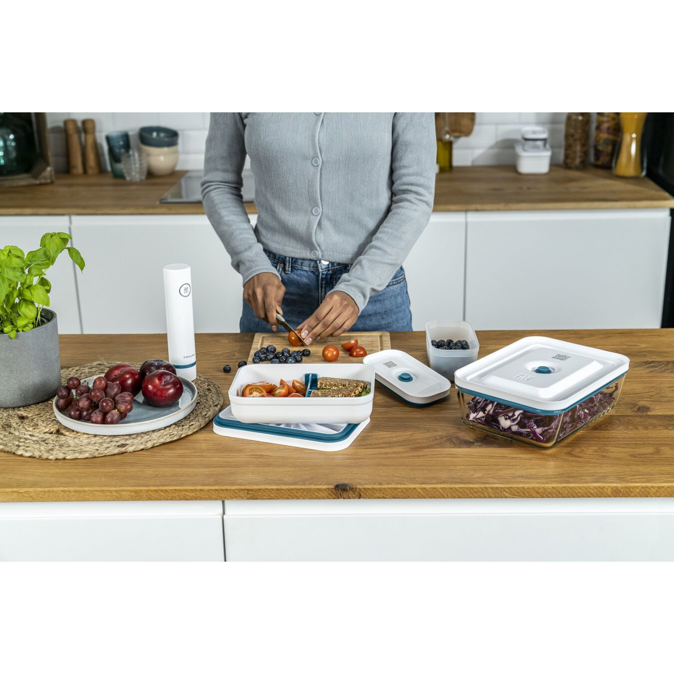 Una persona affetta pomodori su un tagliere in una cucina con frutta fresca e contenitori.