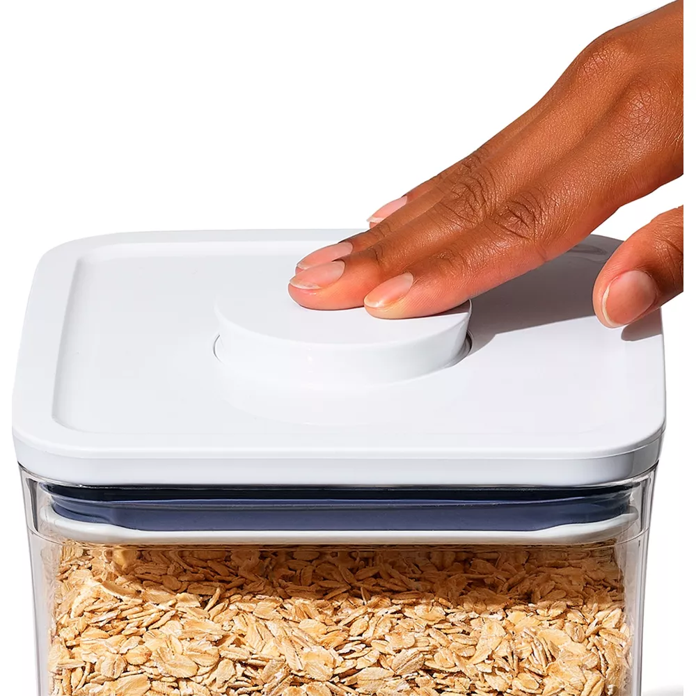 Una mano preme il pulsante rotondo su un contenitore bianco pieno di fiocchi d'avena.