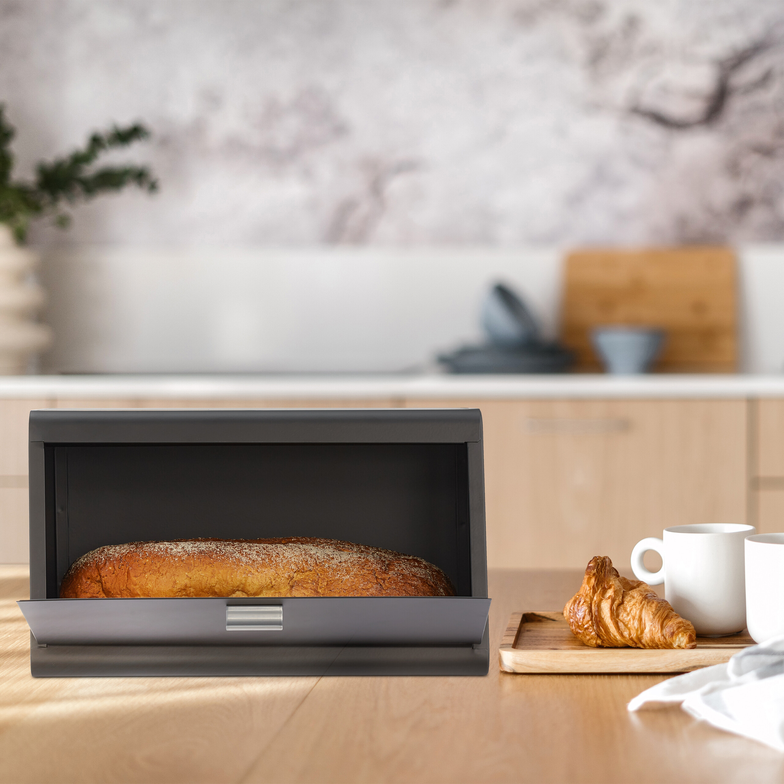 Una portapane grigia con pane fresco si trova su un piano di lavoro in legno in una cucina moderna.
