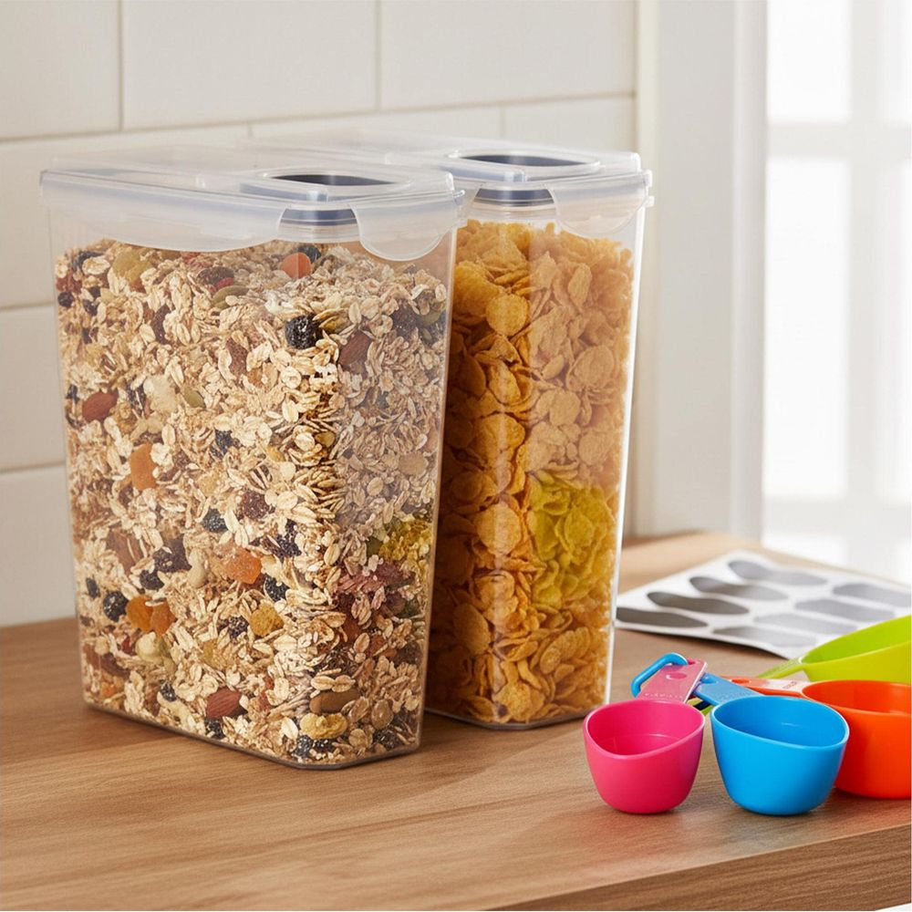 Zwei große transparente Behälter mit Müsli und Cornflakes stehen auf einer Holzoberfläche mit bunten Messbechern.