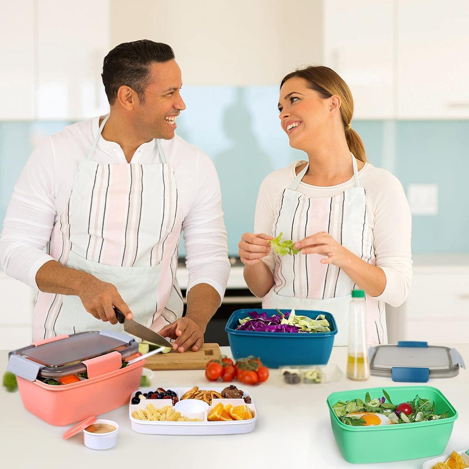 Felice coppia con grembiuli prepara insalata fresca in cucina, circondata da colorati portapranzo.