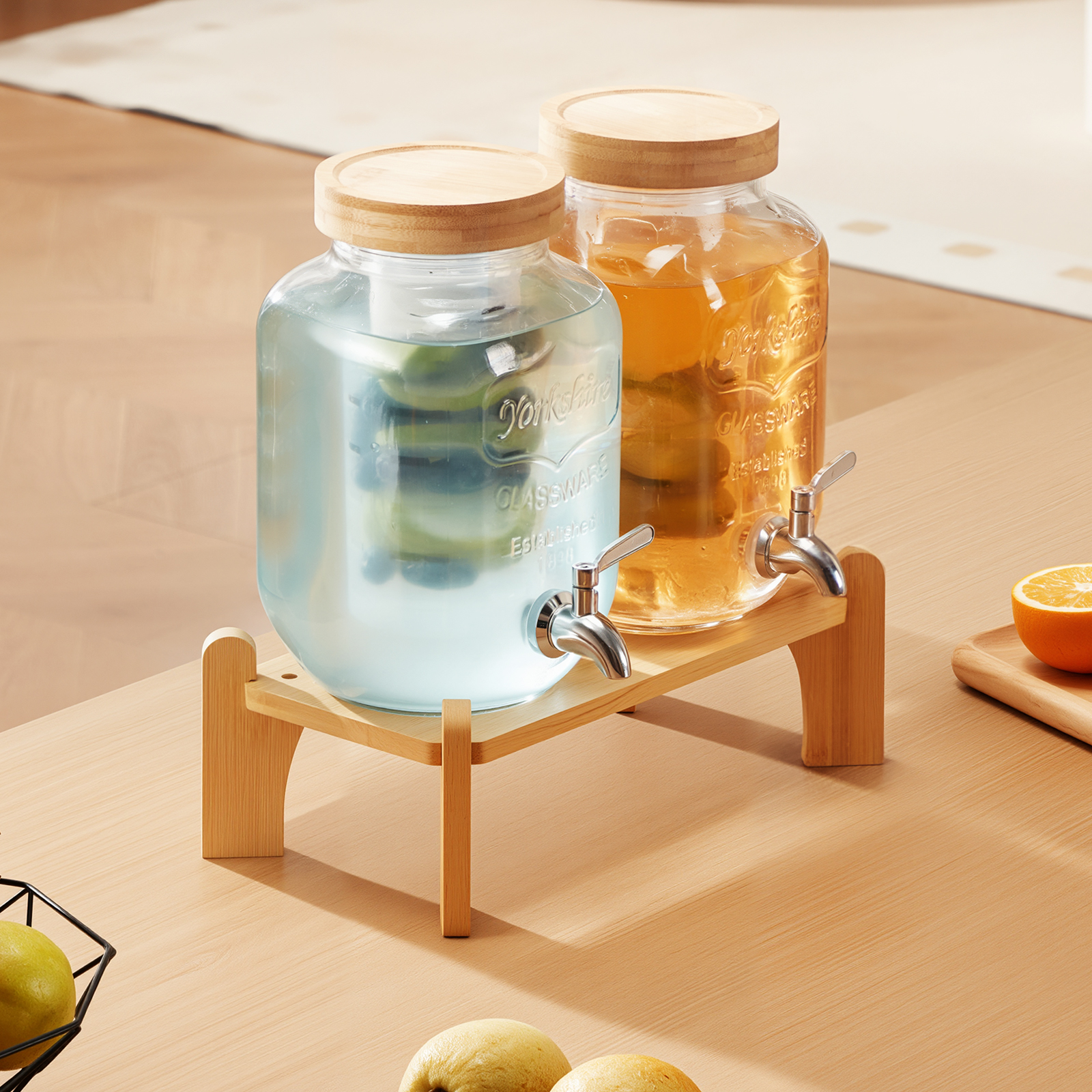 Dos dispensadores de vidrio con tapas y grifos de madera sobre un soporte de madera, rodeados de cítricos.