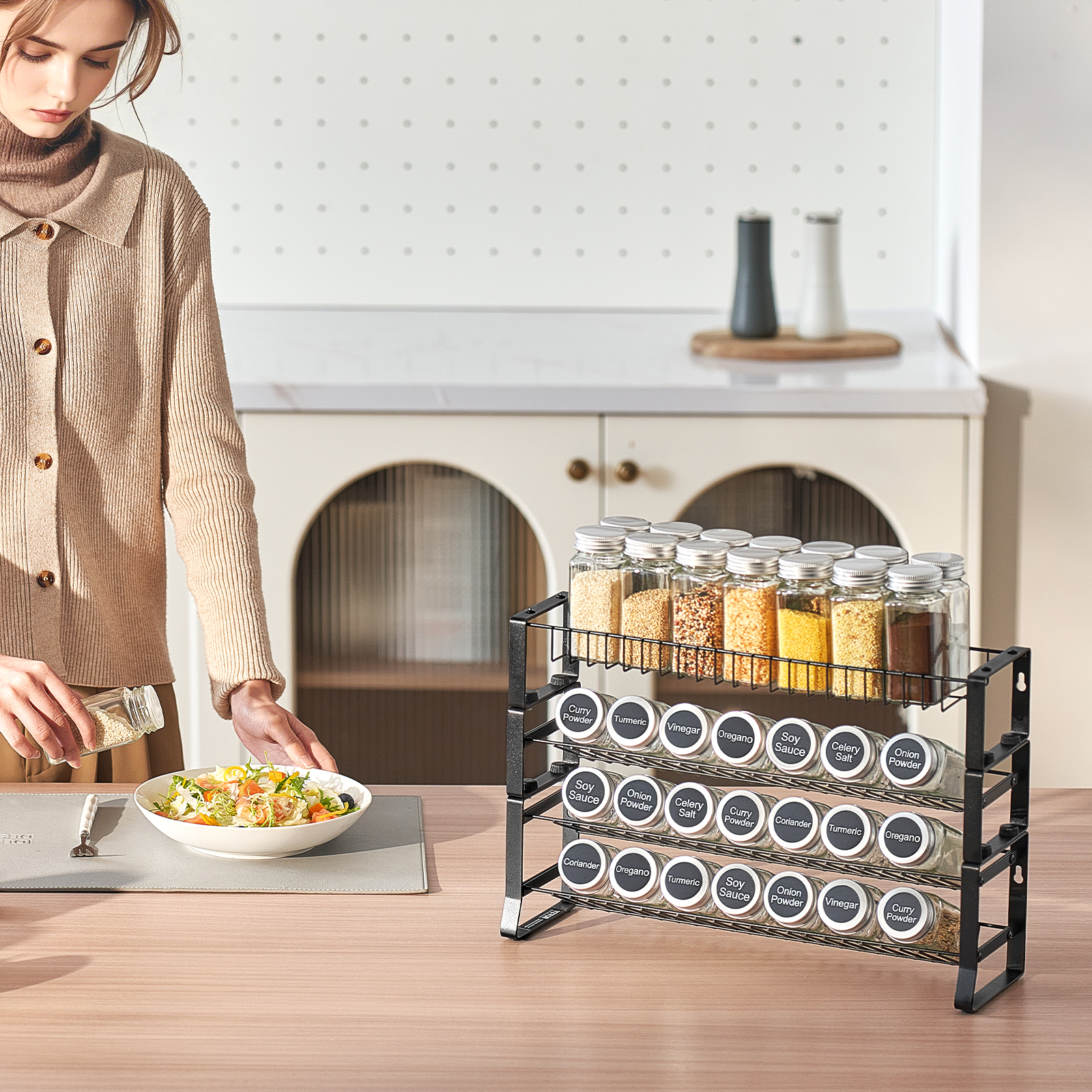 Una donna con un maglione marrone condisce un'insalata vicino a una spezieria in cucina.